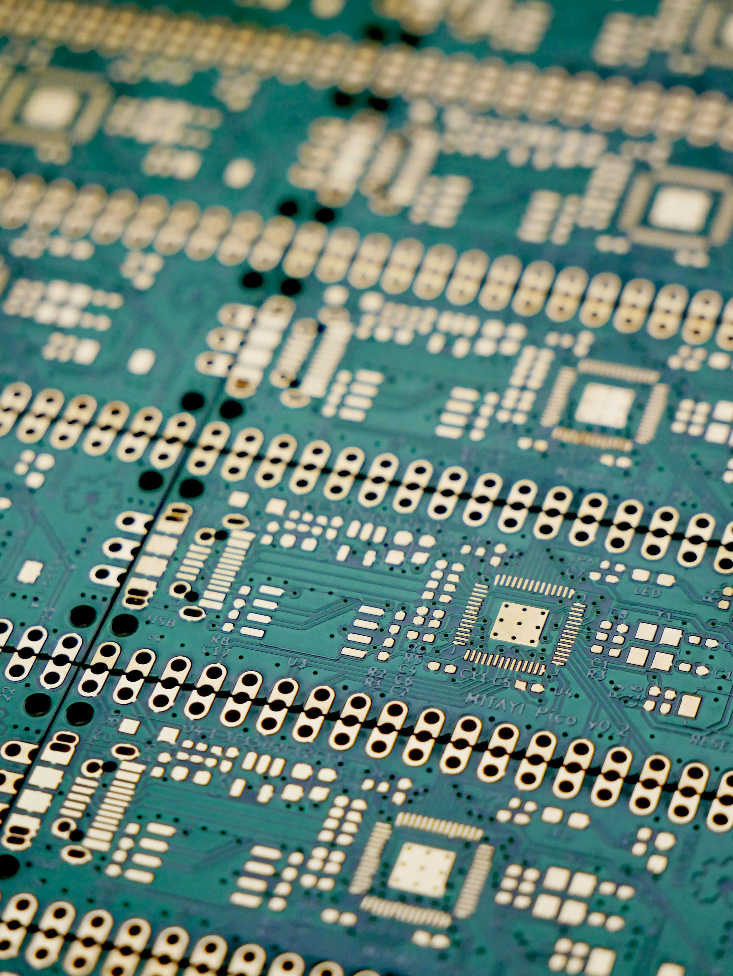 Close-up of a green printed circuit board with various white and gold electronic components and pathways.