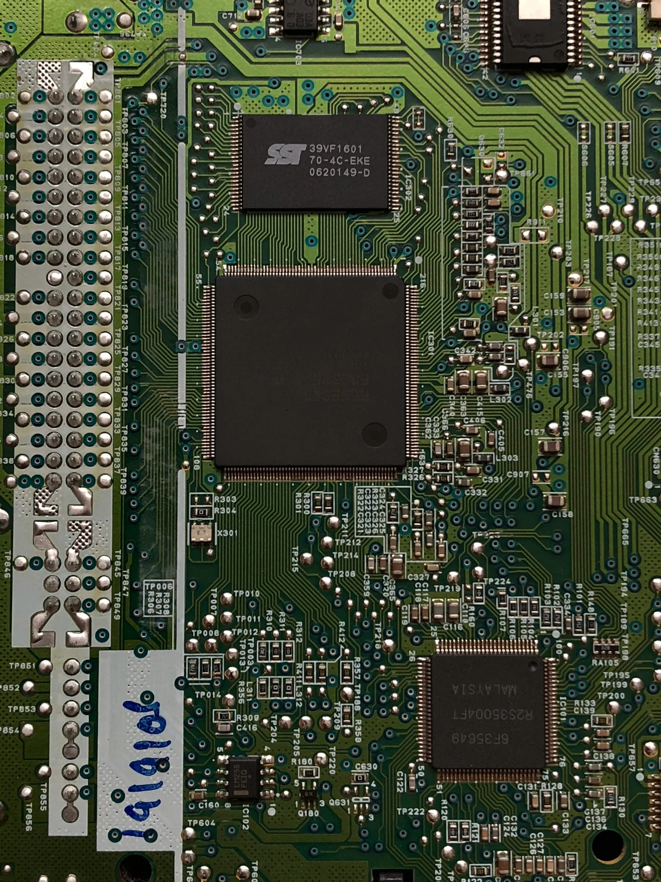 A close-up of a green printed circuit board (PCB) with multiple electronic components, including integrated circuits, capacitors, resistors, and solder points.