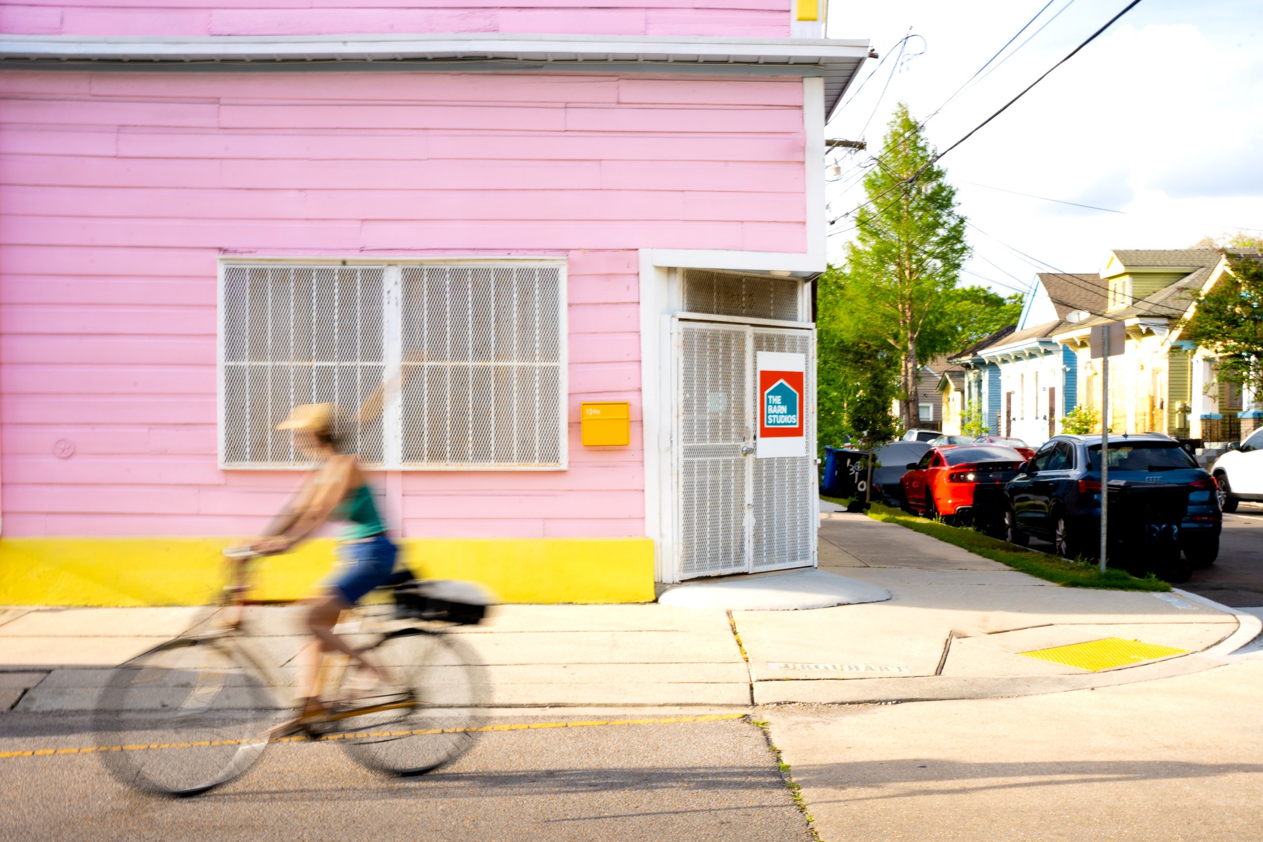 A person riding a bicycle past a pink building with yellow accents in an urban neighborhood.