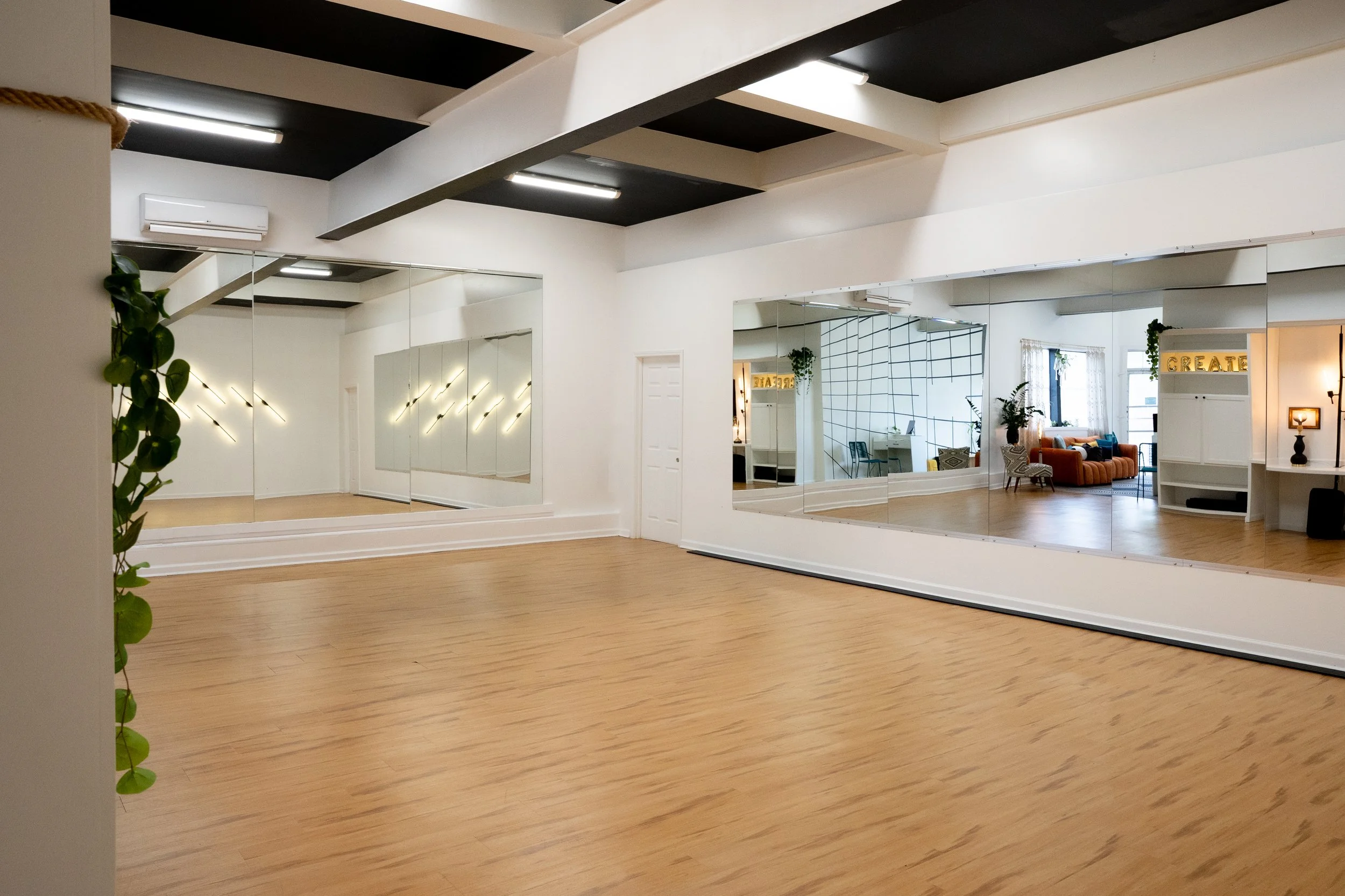Empty dance studio with wooden floor, large mirrors on the wall, and a small green plant to the side.