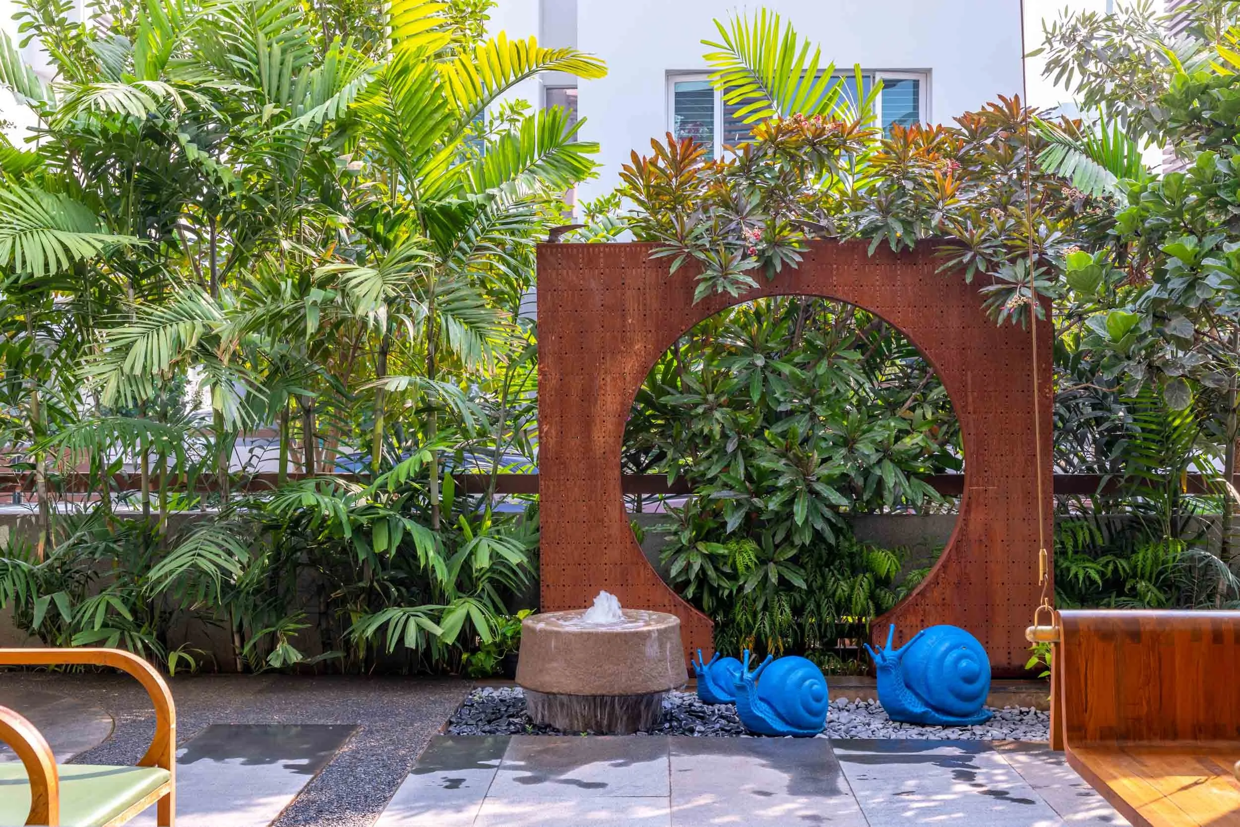 Modern outdoor courtyard featuring a circular architectural feature wall, lush tropical plants, and dark stone paving