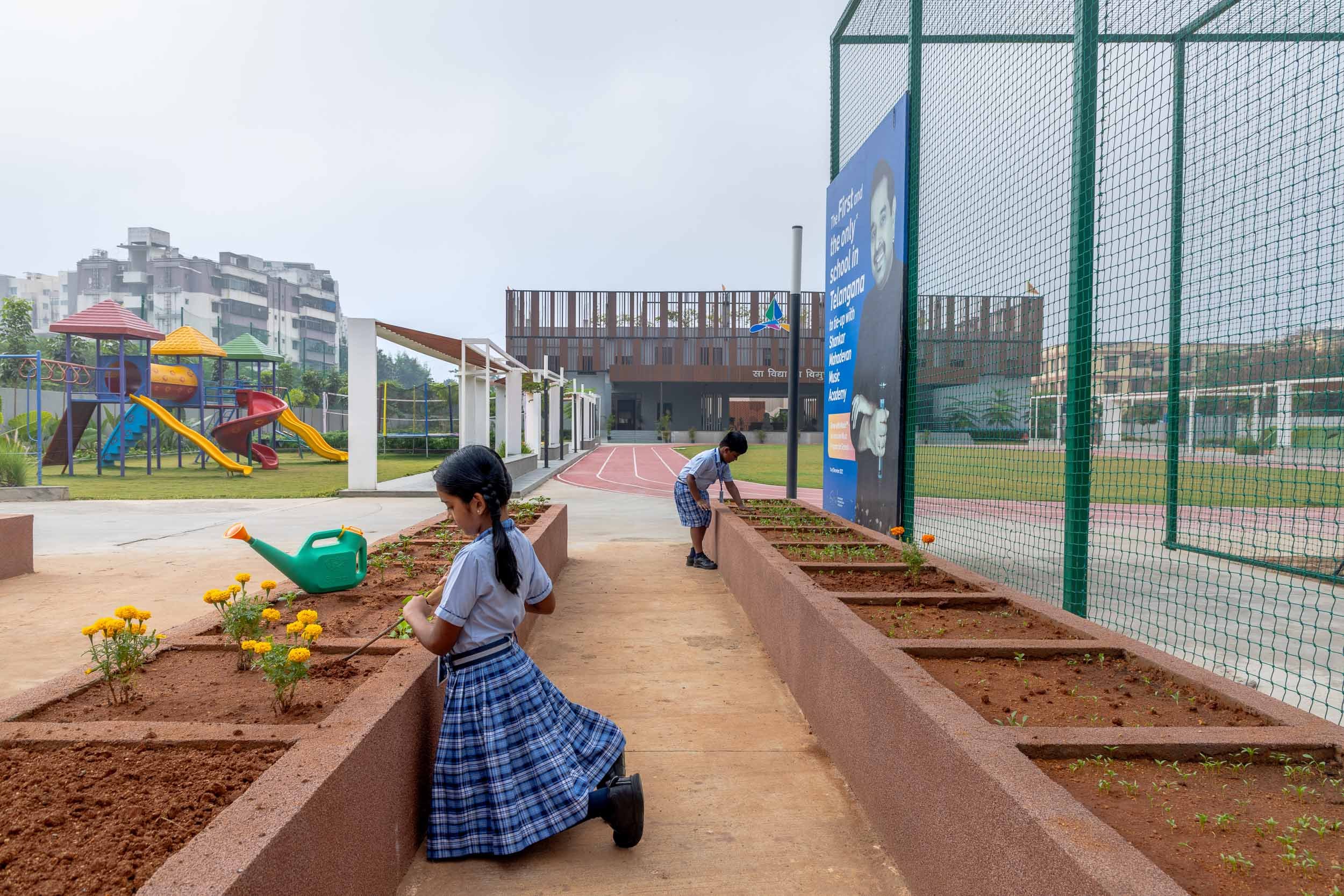 Exterior school photography of a young student running along a landscaped campus pathway near an outdoor playground