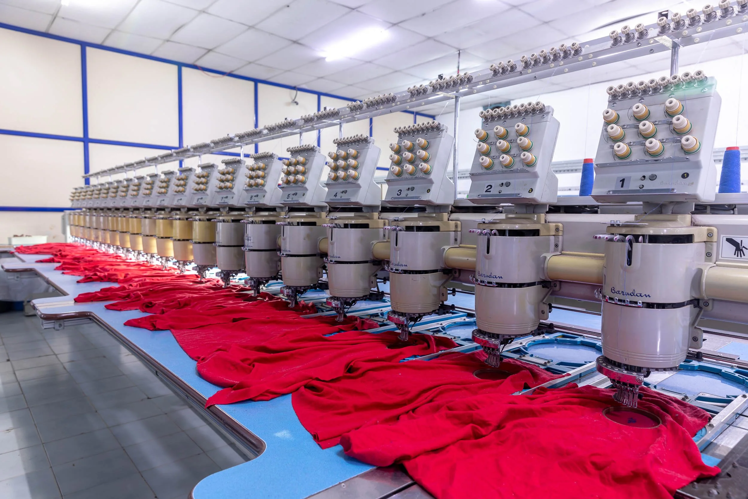 Interior industrial photography of a long production line in a textile manufacturing plant, featuring heavy machinery processing vibrant red fabric