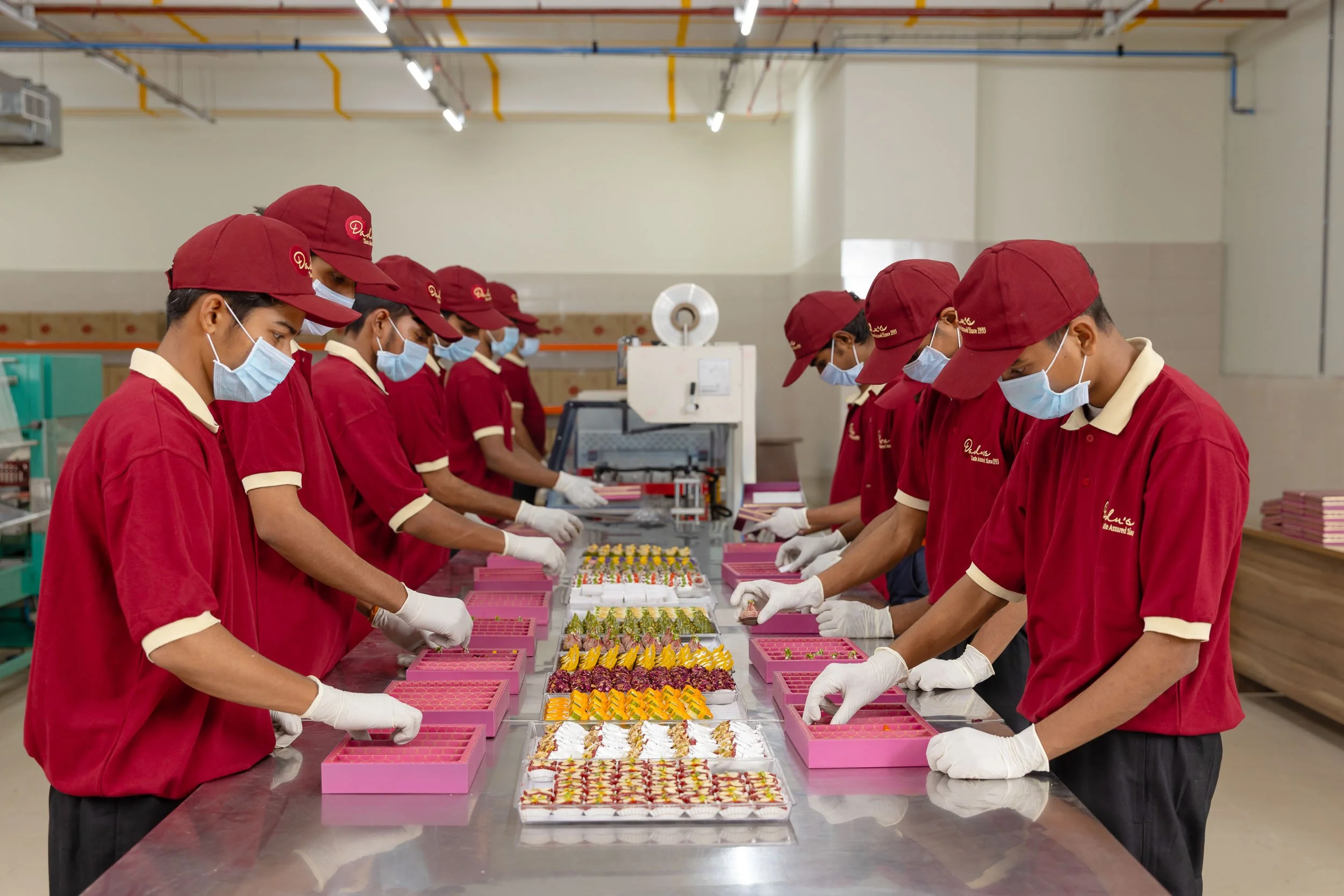 Interior industrial photography of workers in red sanitary uniforms and masks packaging products on a stainless steel assembly line in a manufacturing facility