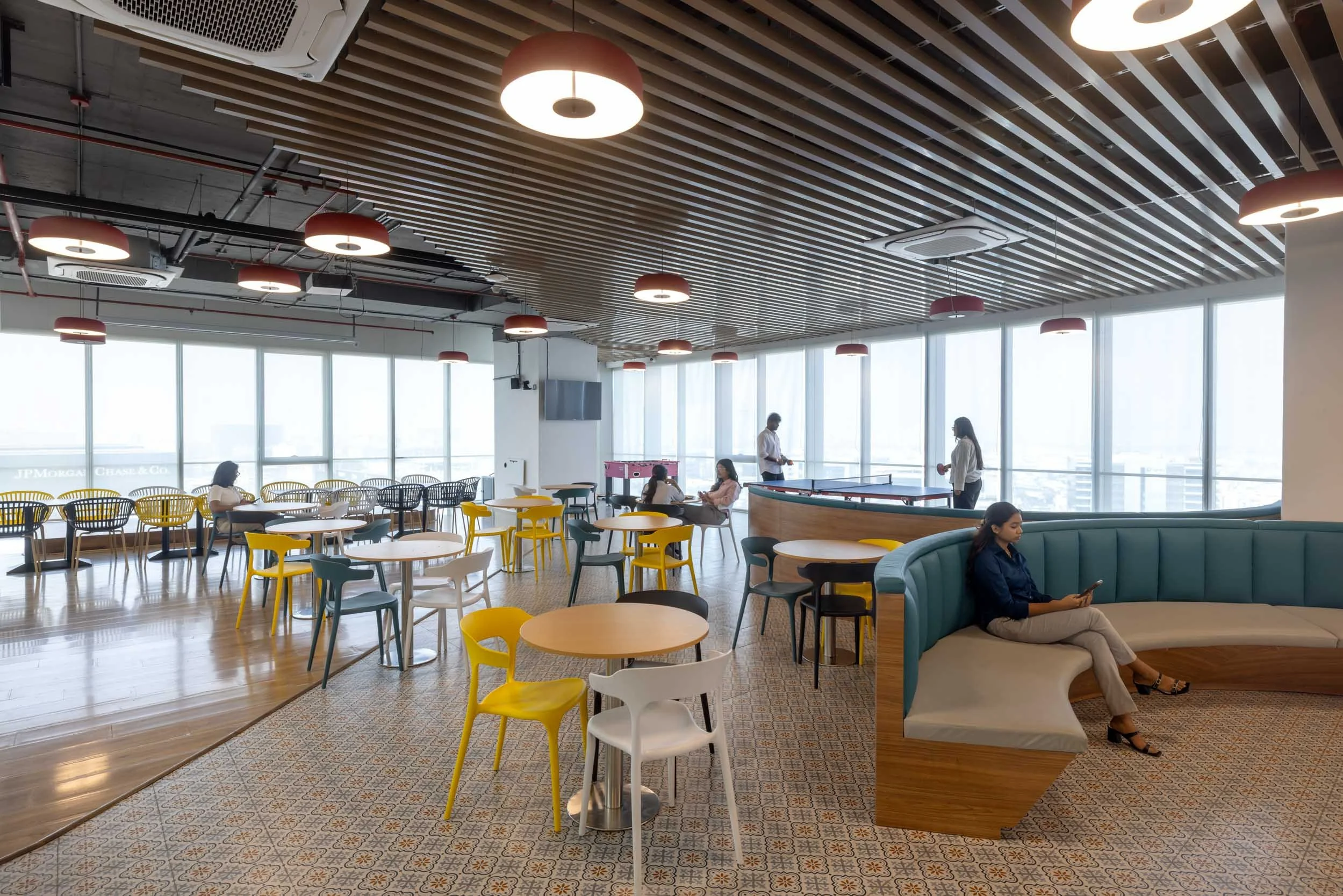 Commercial interior photography showcasing a modern corporate dining and breakout space, highlighting custom architectural ceiling design, vibrant cafeteria seating, and natural lighting.
