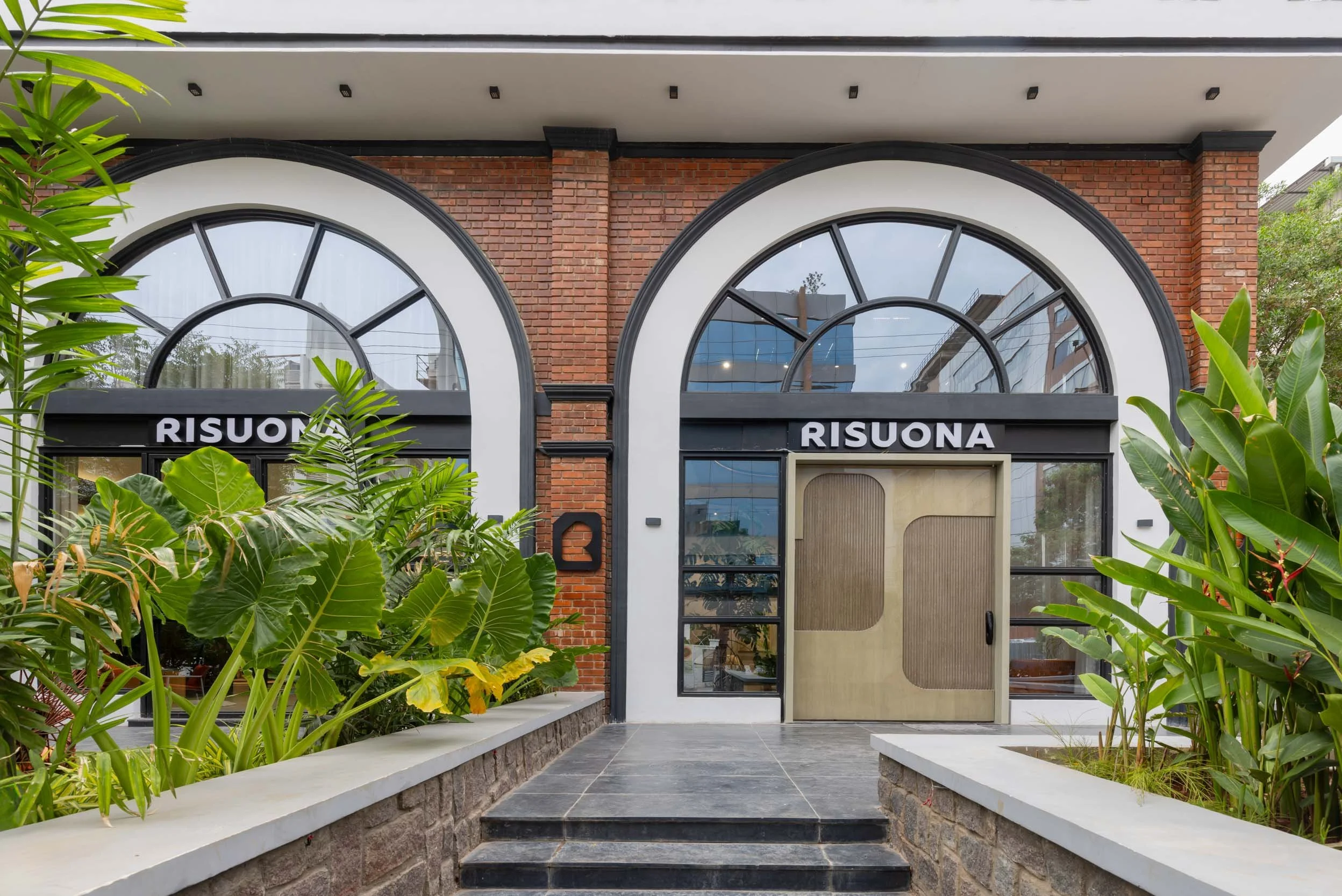Professional commercial architecture photography capturing an inviting storefront exterior, highlighting a warm brick facade, elegant arched entrances, and a beautifully landscaped approach