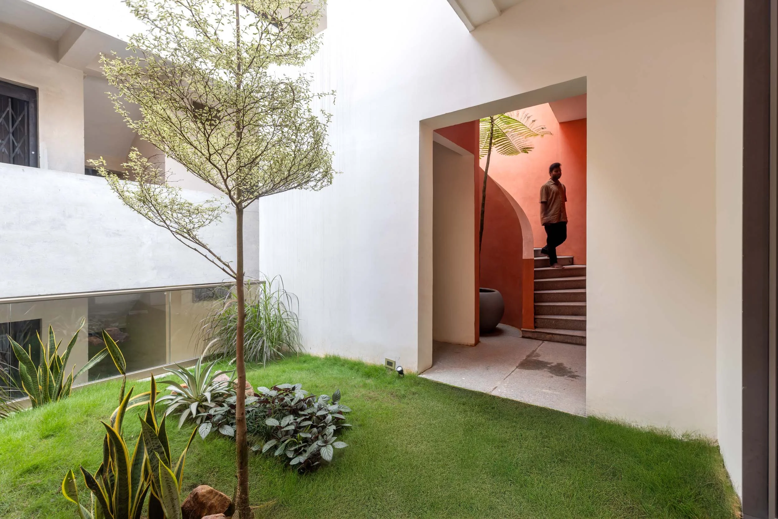 Professional exterior architectural photography of a modern residential home, highlighting a landscaped inner courtyard and a striking terracotta entryway