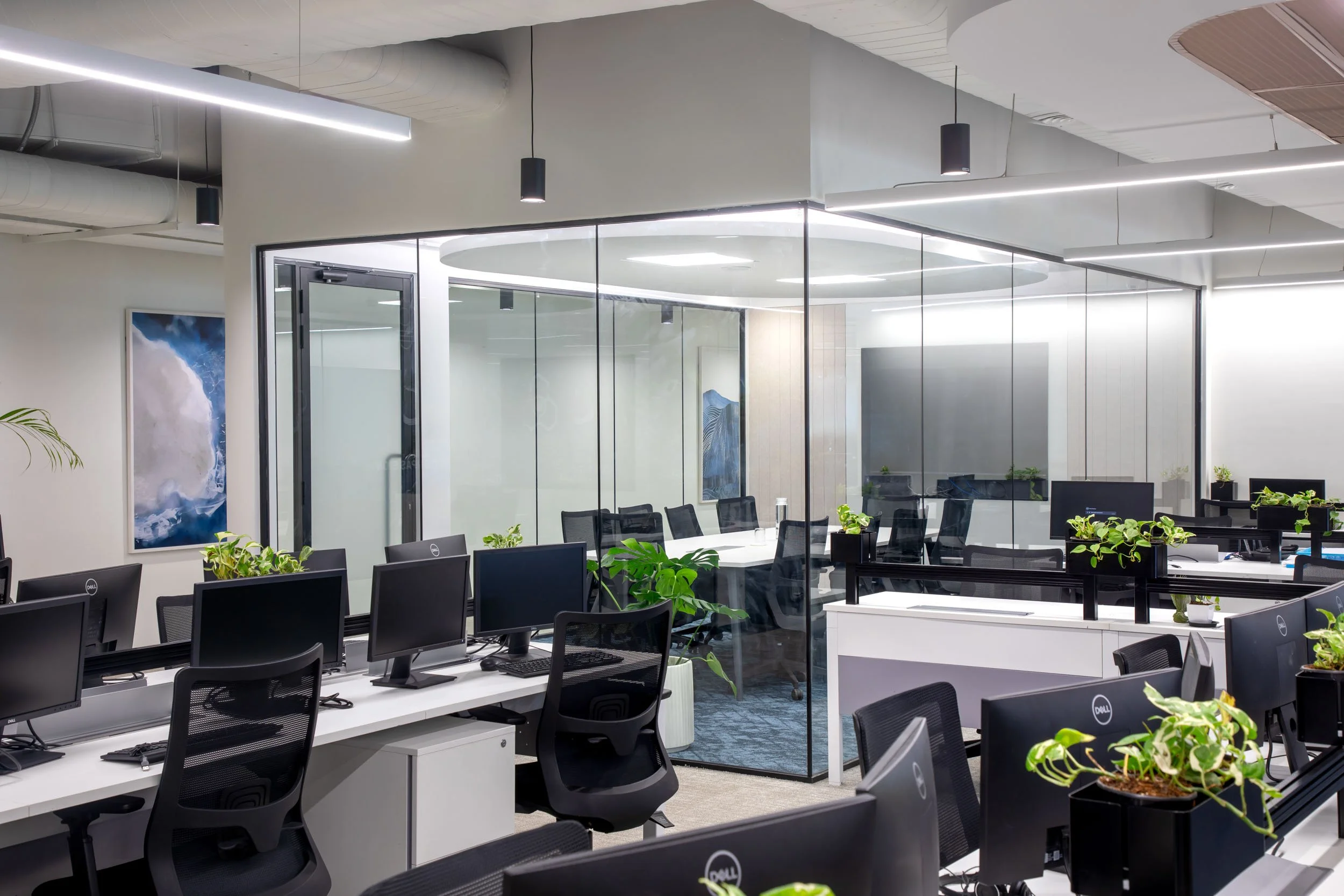 Commercial interior photography showcasing a dynamic office hallway, highlighting transparent glass-enclosed workspaces, dark industrial ceilings, and vibrant yellow lounge seating.