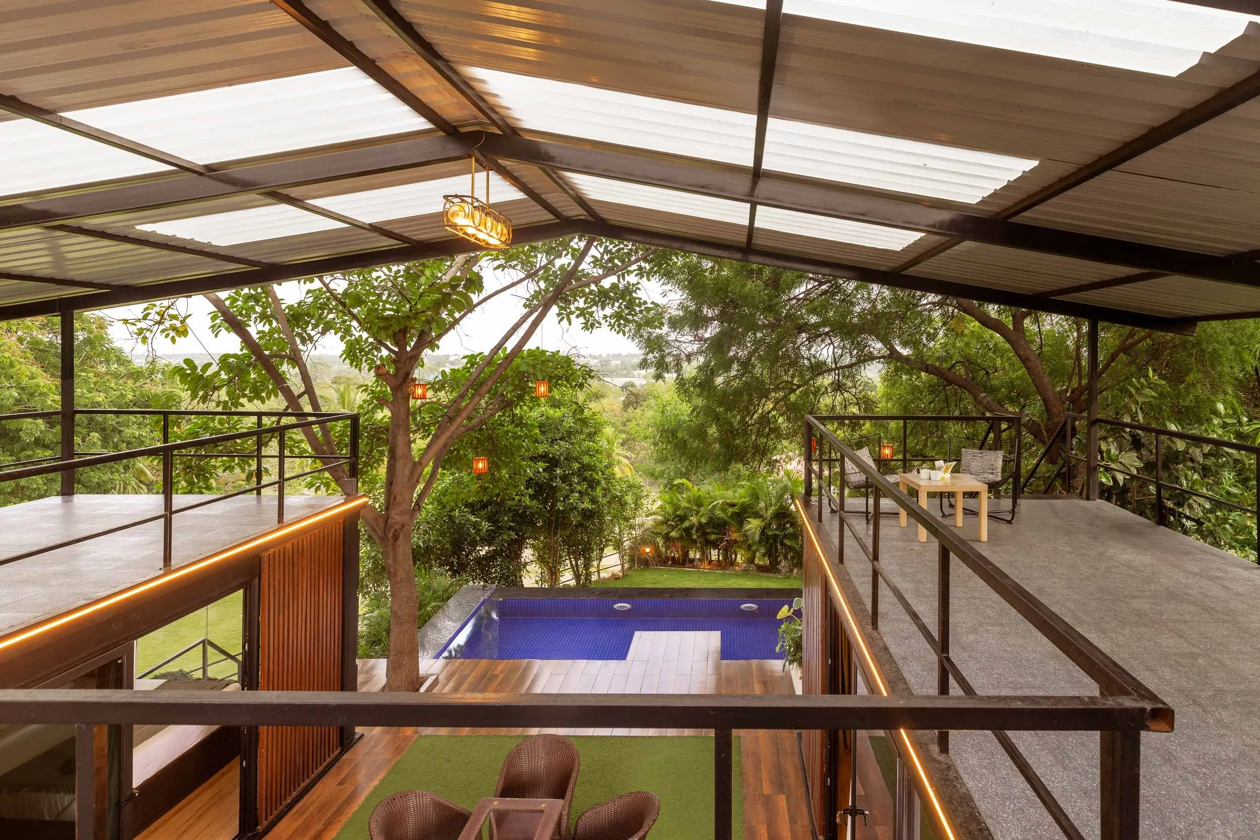Exterior daytime photography of a modern luxury staycation in Hyderabad, featuring a covered deck overlooking a private plunge pool and lush trees