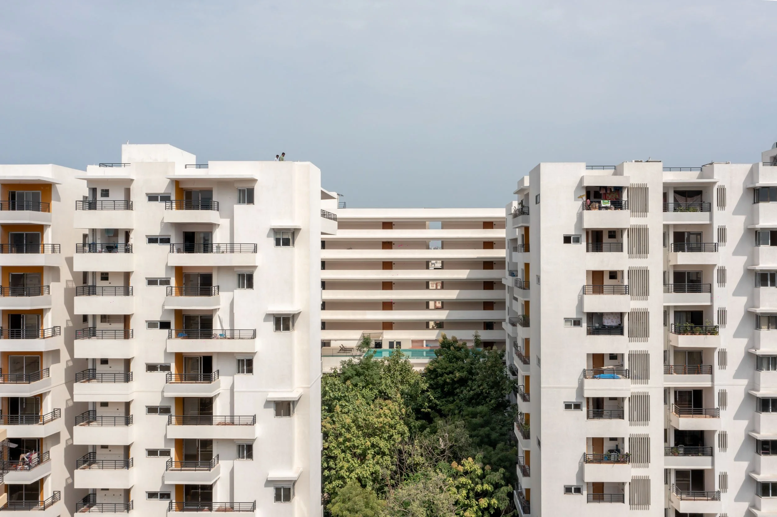 Residential real estate exterior photography showcasing twin modern apartment blocks and integrated green landscaping under a clear blue sky.