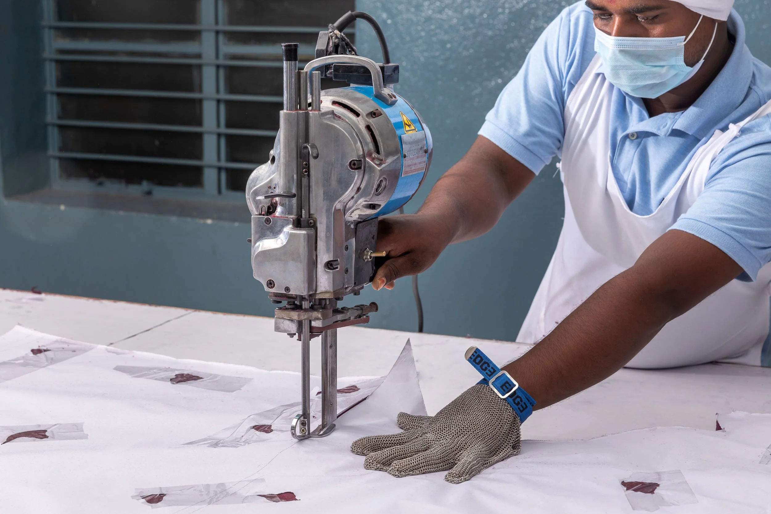 Interior industrial photography of a skilled textile factory worker operating a vertical fabric cutting machine on a stack of white material