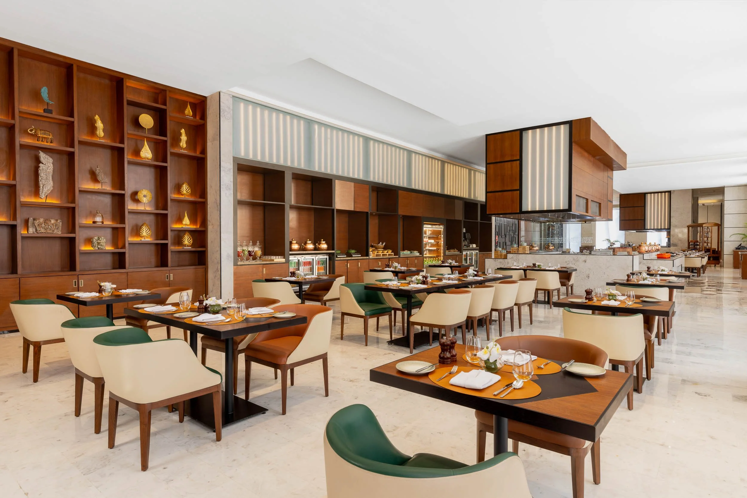 Interior photography of a bright, modern hotel restaurant featuring wooden dining tables, upholstered chairs, custom wooden shelving, and a slatted ceiling design