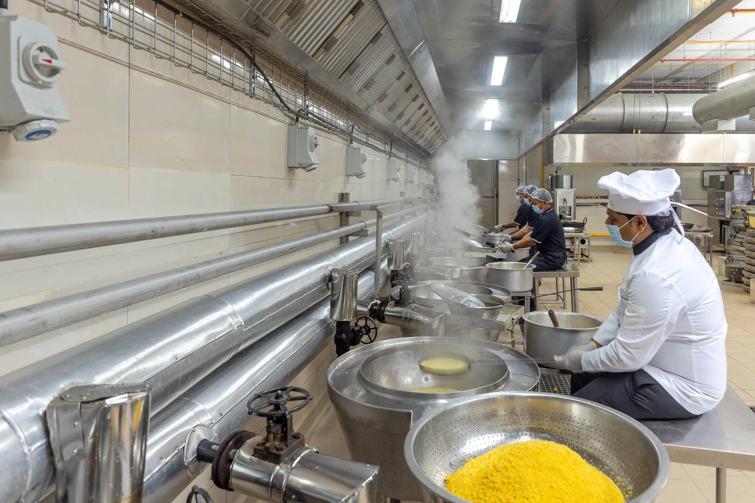 Interior industrial photography of a worker in white sanitary gear processing bright yellow food ingredients in stainless steel bowls on a commercial production line