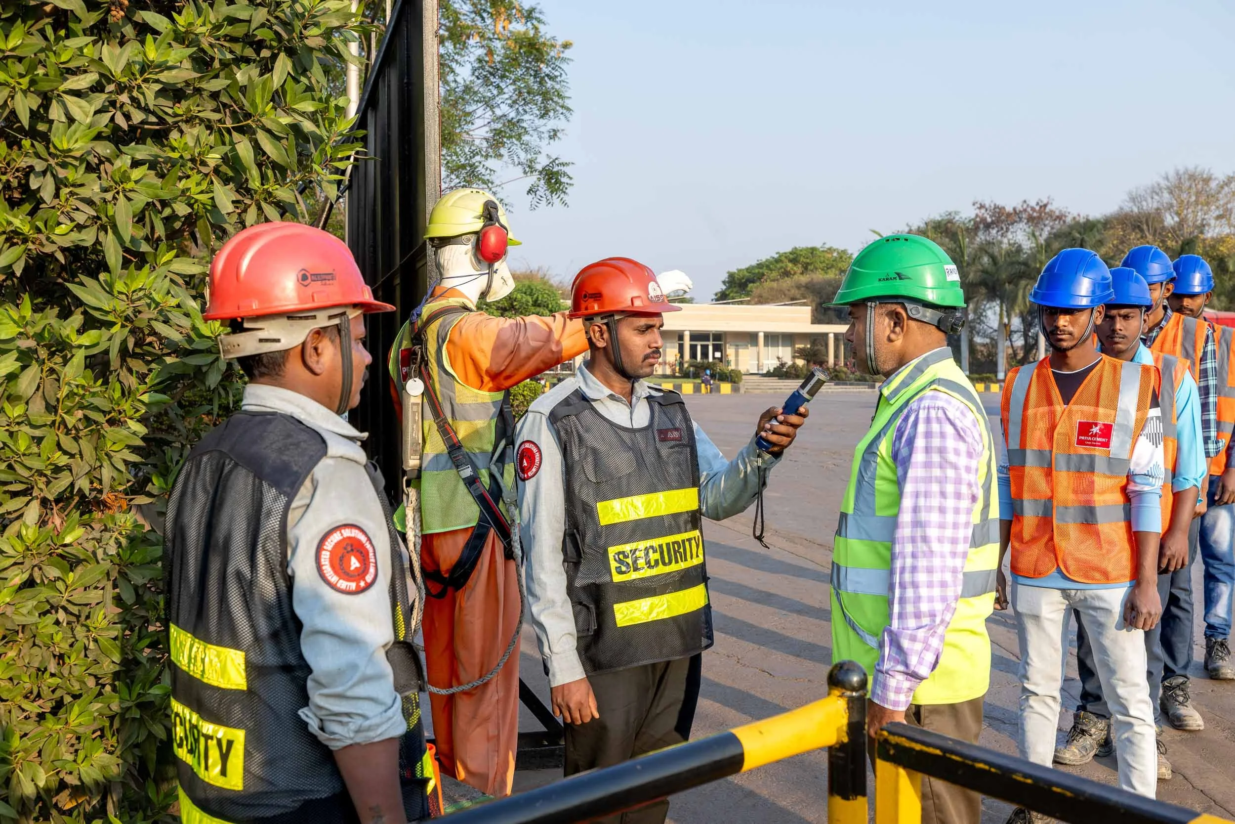 Exterior industrial photography of plant workers and engineers in hard hats and safety vests having an on-site meeting at a manufacturing facility in India