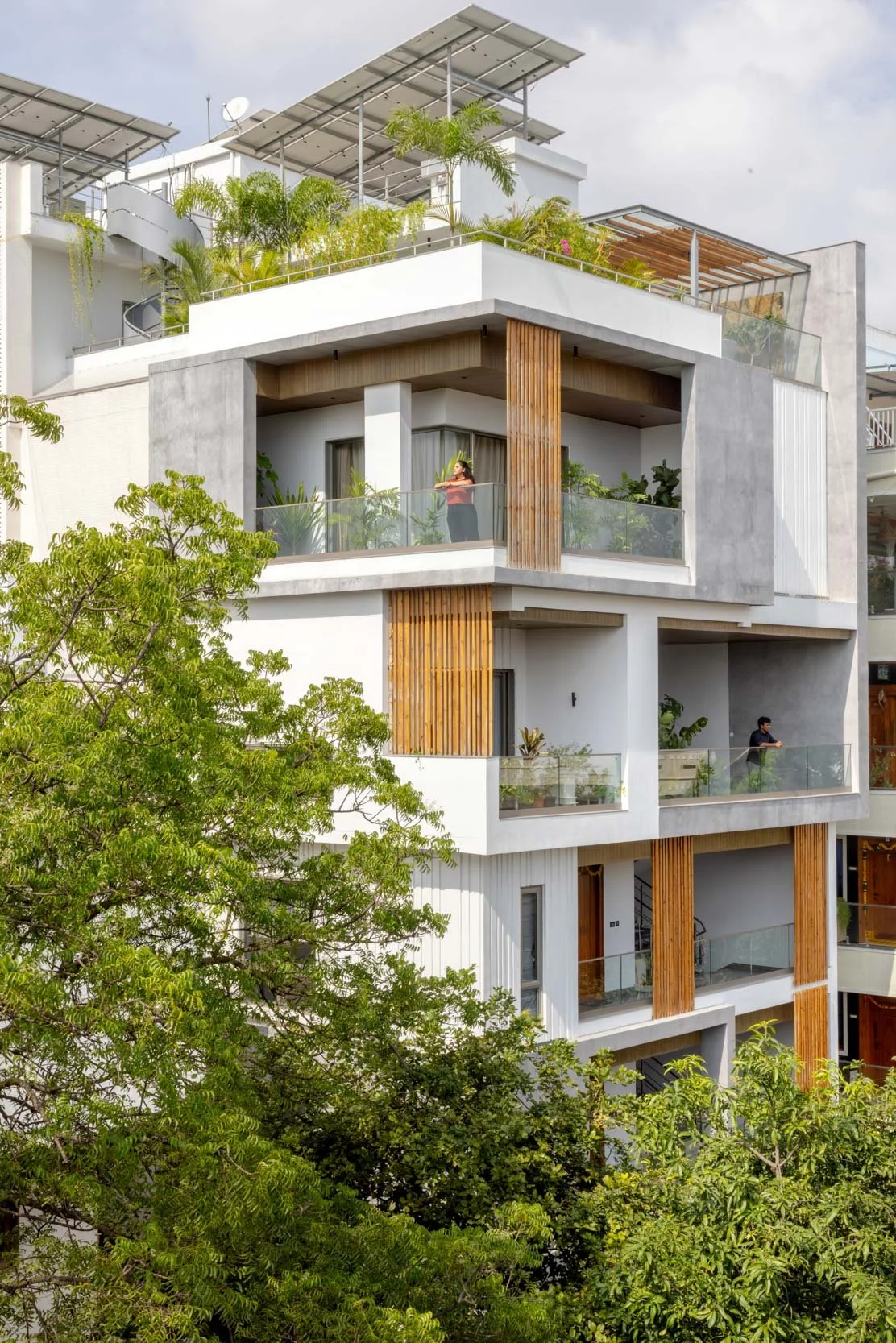 Professional exterior architectural photography of a modern multi-story residential home, highlighting a clean white facade with warm wooden accents and lush balcony greenery