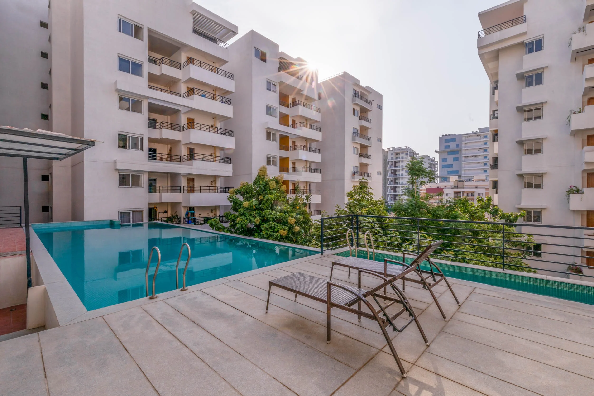 Residential real estate photography highlighting luxury community amenities, featuring a large outdoor swimming pool, poolside loungers, and modern apartment architecture