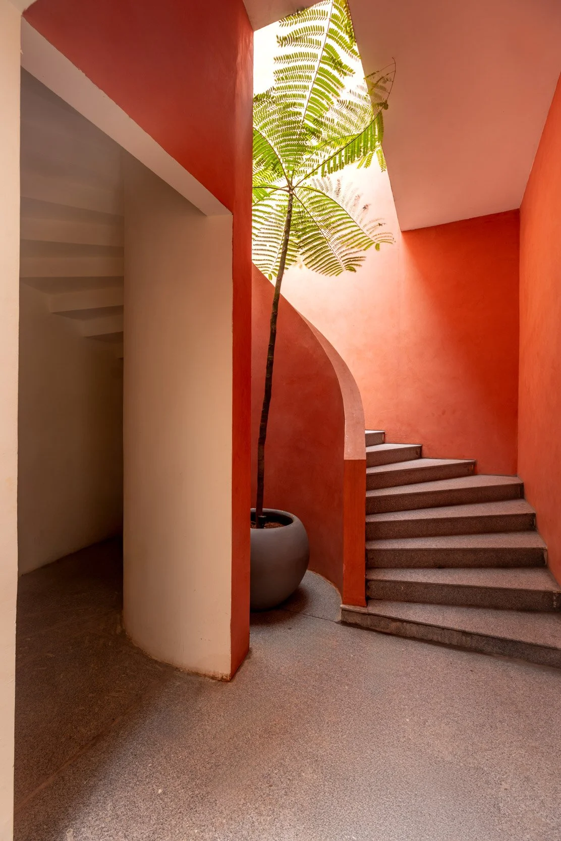 Professional interior architectural photography highlighting a vibrant terracotta residential stairwell with dramatic natural lighting and shadows.