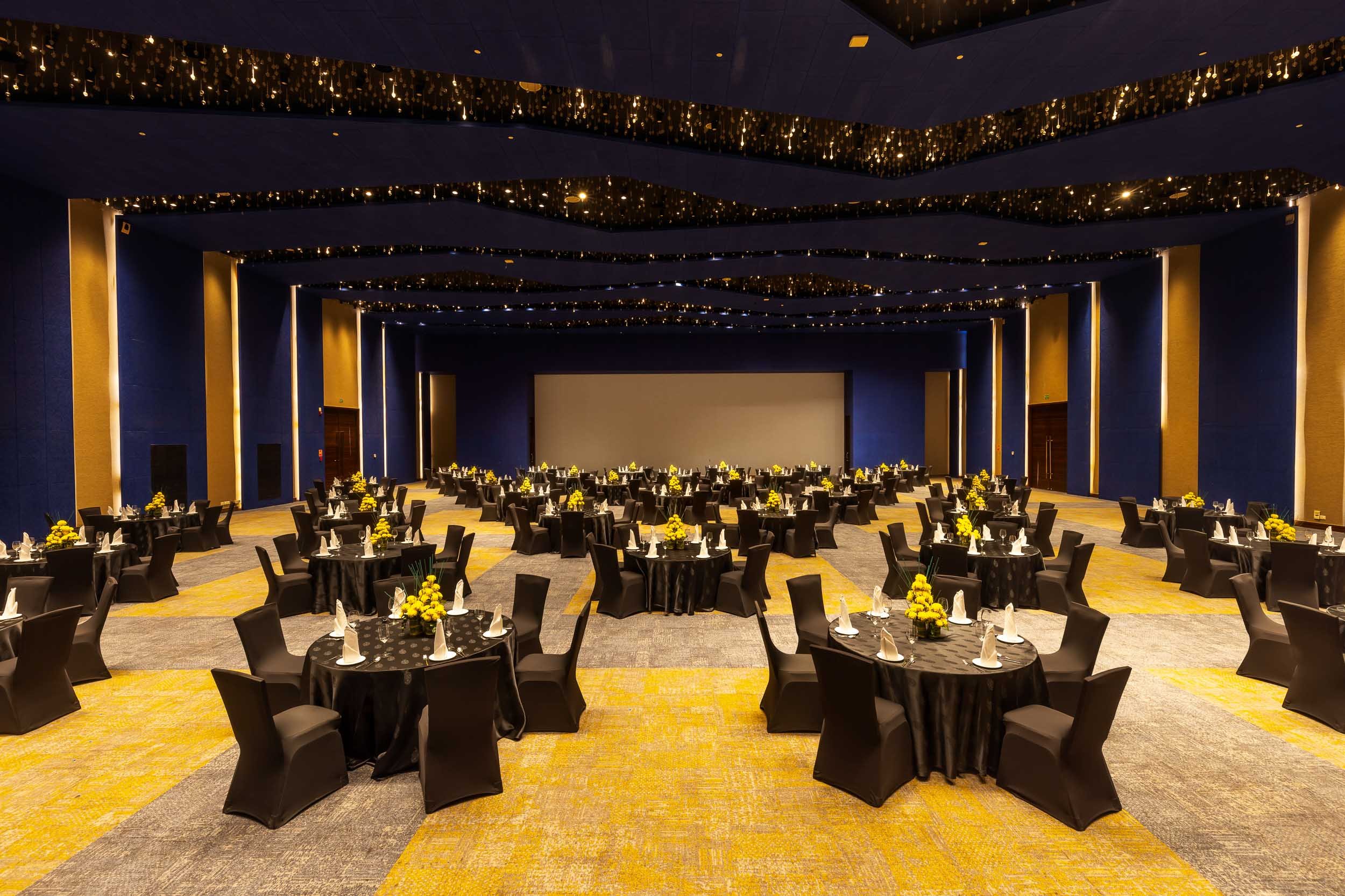 Interior photography of a grand hotel banquet hall set up for a formal event, featuring round dining tables with black linens, gold chairs, deep blue walls, and a starry night ceiling