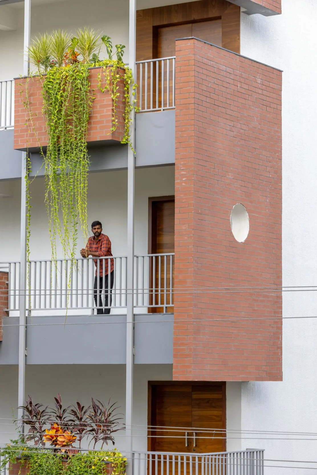 Professional architectural photography capturing a modern exterior balcony detail, highlighting a textured terracotta wall panel, trailing greenery, and a sense of human scale