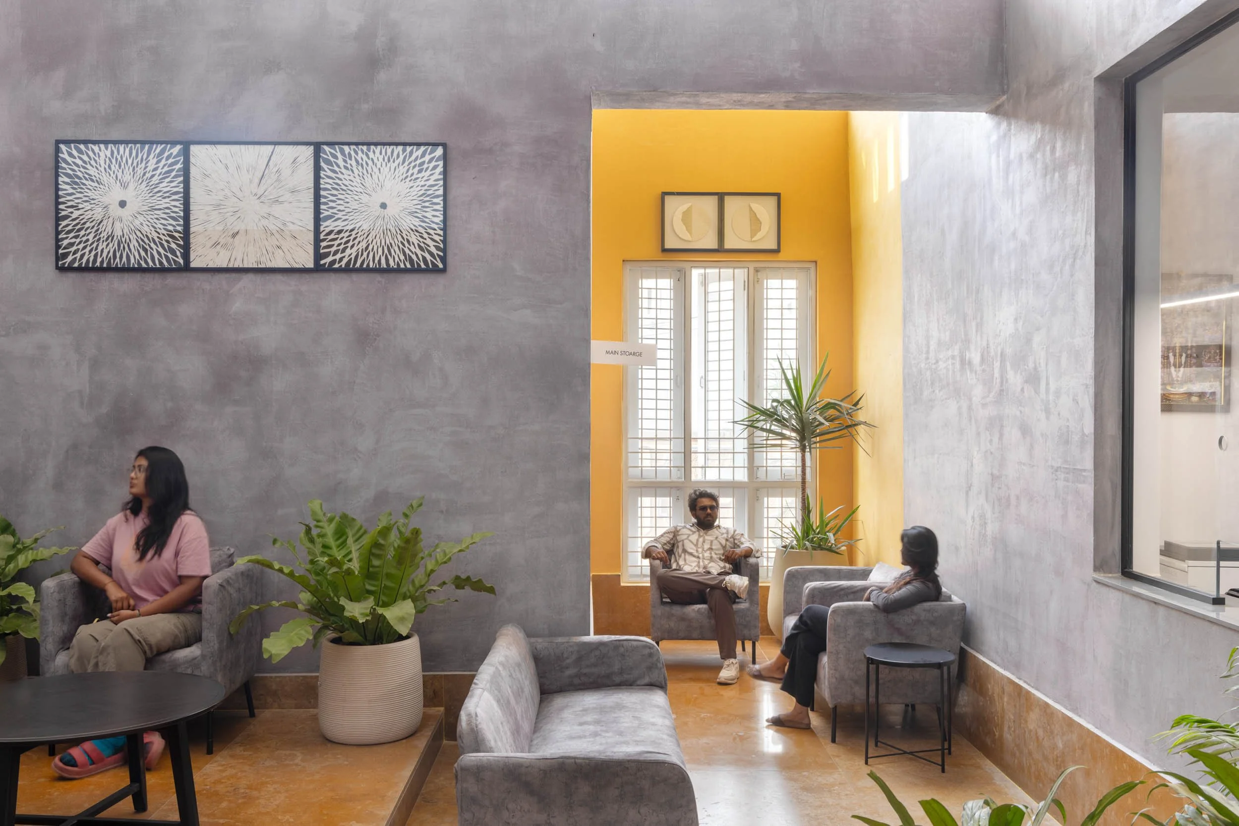 Professional interior architecture photography of a modern commercial lounge, highlighting textured grey walls, vibrant yellow accents, and an inviting seating area with a sense of human scale.