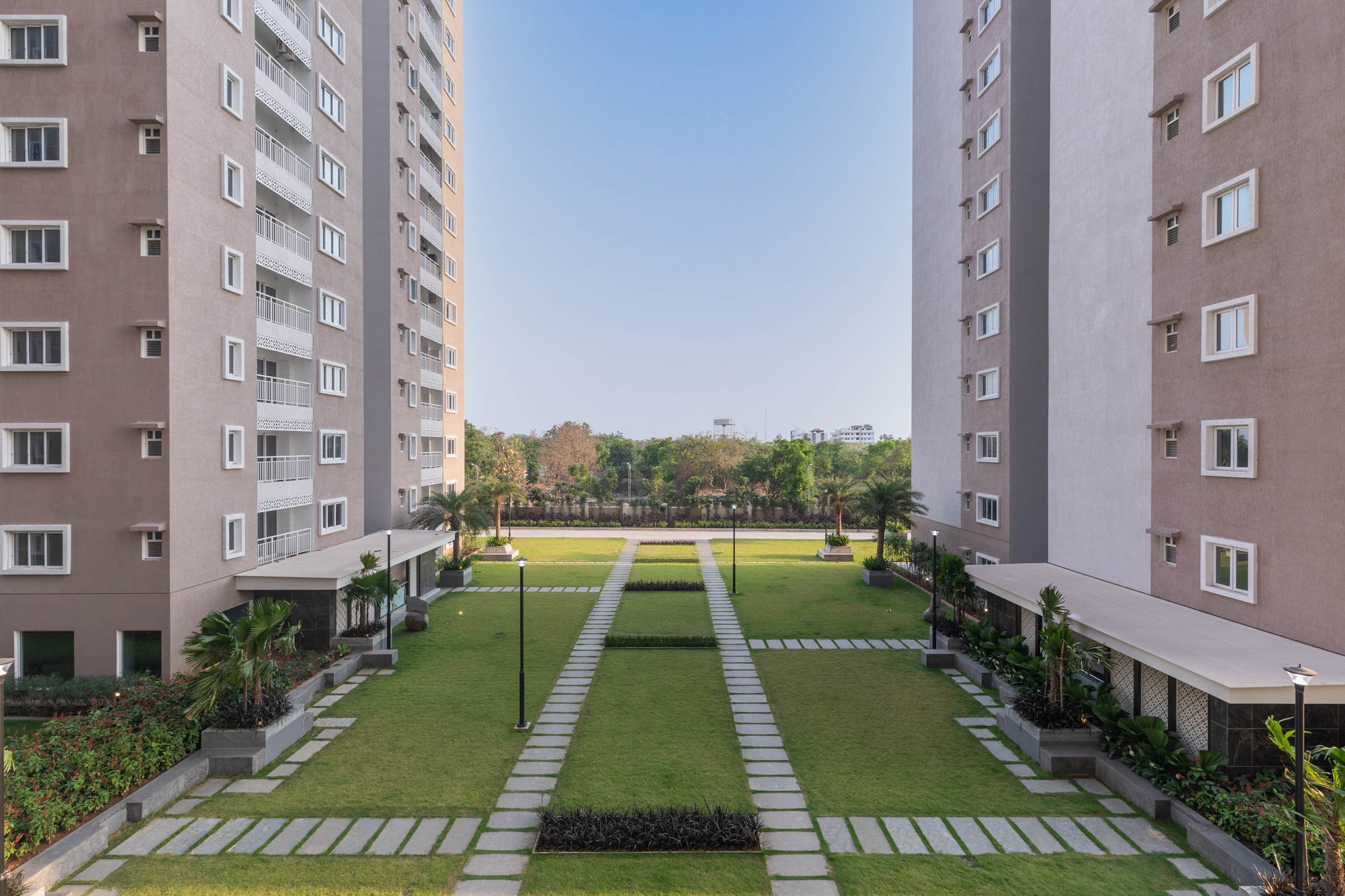 Residential real estate photography showcasing modern apartment buildings flanking a lush, green central courtyard and stone walkway