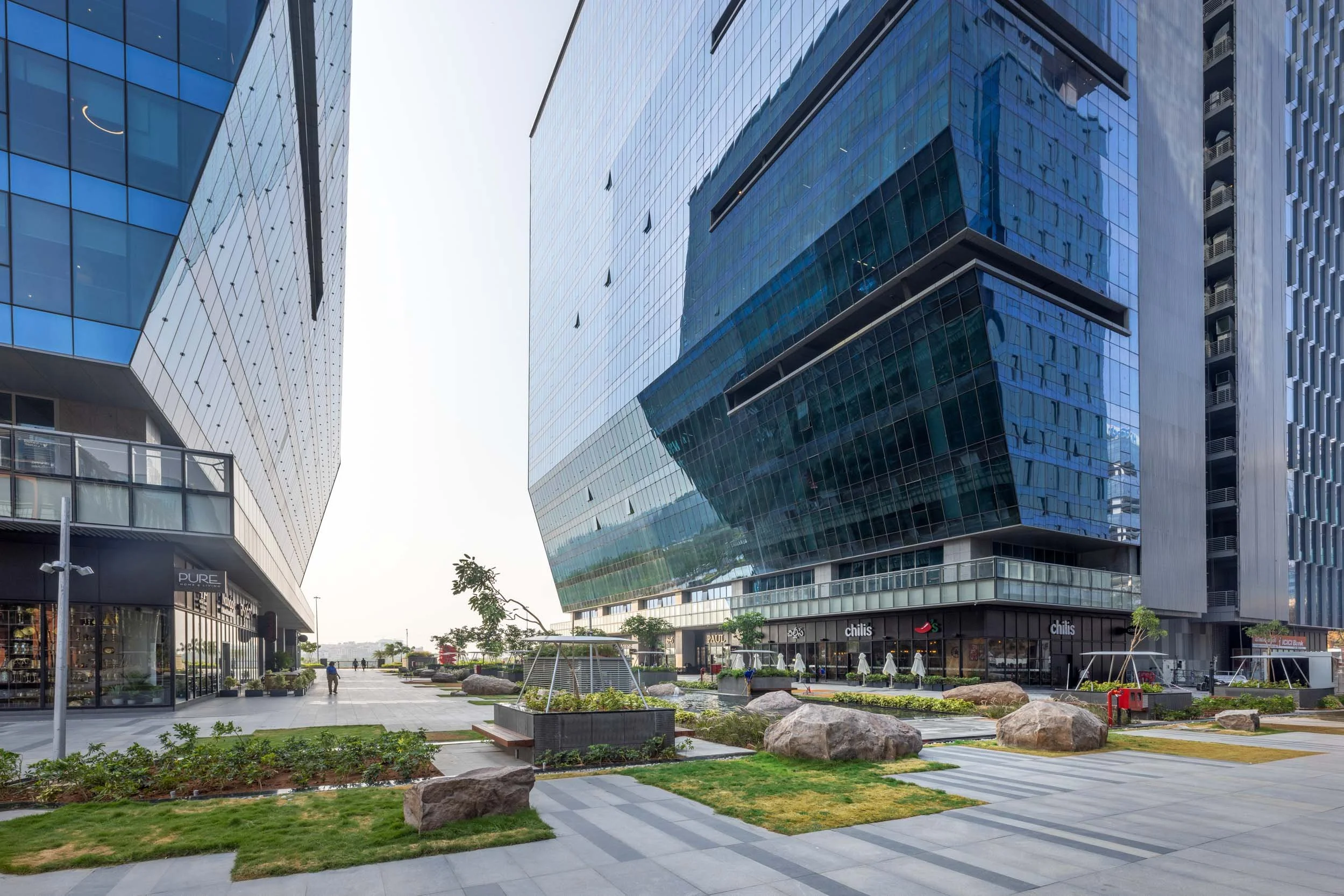 Professional commercial architecture photography capturing a ground-level perspective of a modern business park, highlighting sleek glass facades and an integrated pedestrian plaza