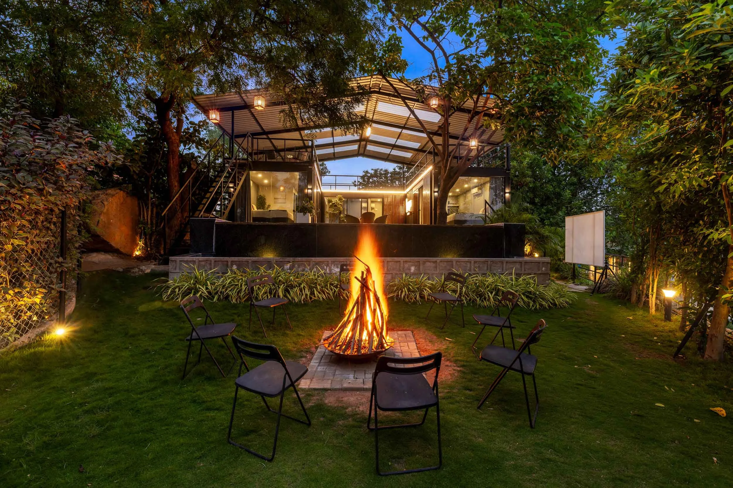 Nighttime exterior shot of a luxury staycation fire pit area in Hyderabad, surrounded by outdoor seating and illuminated trees