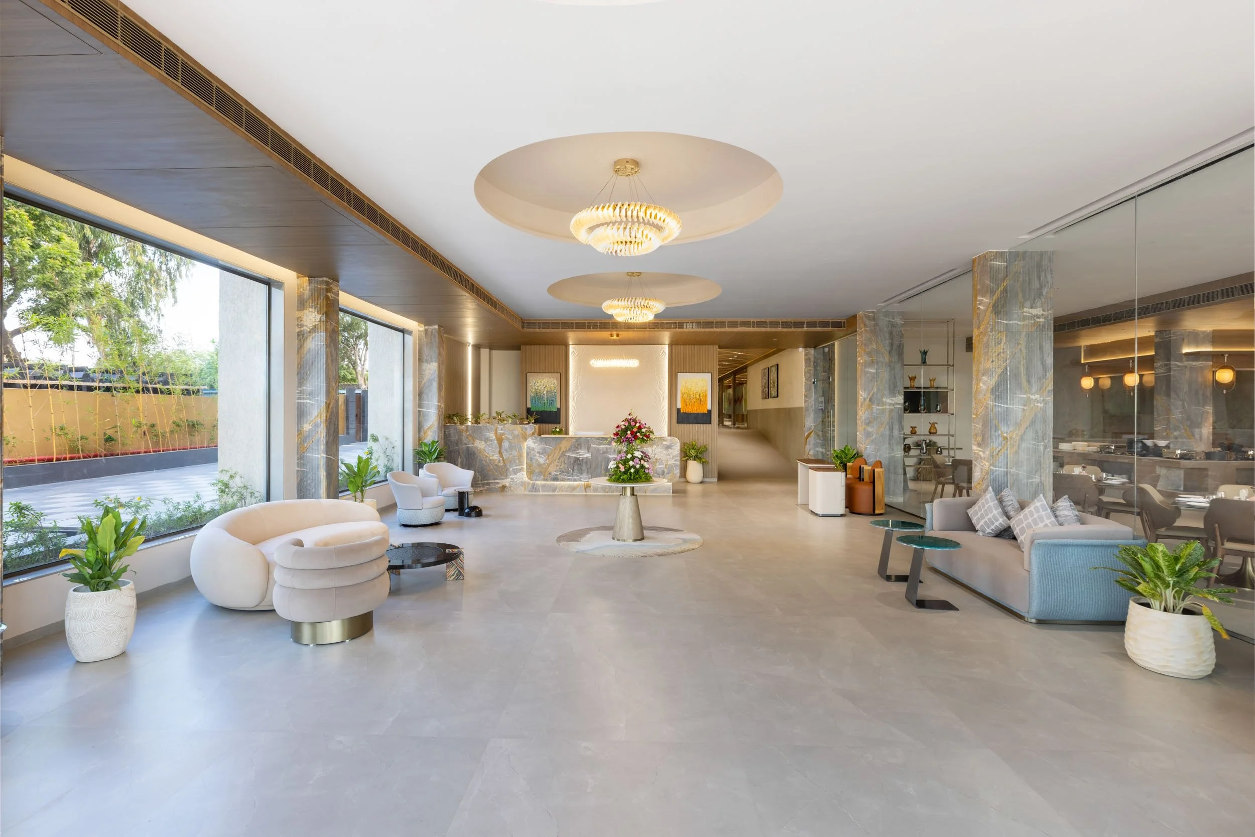 Interior photography of a spacious luxury hotel lobby featuring large windows, modern lounge seating, polished flooring, and circular ceiling lights
