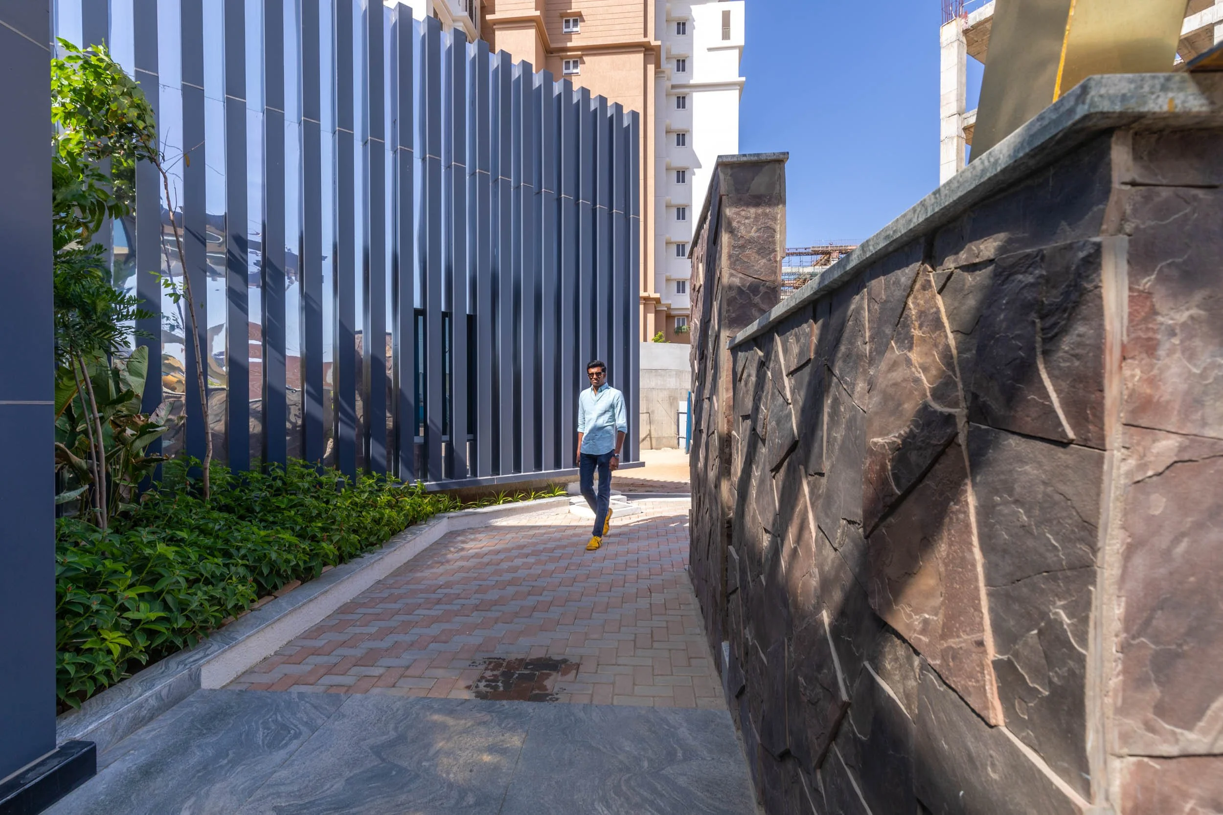 Commercial exterior architecture photography showcasing a landscaped pedestrian pathway, featuring contrasting modern vertical fins and natural stone elements.