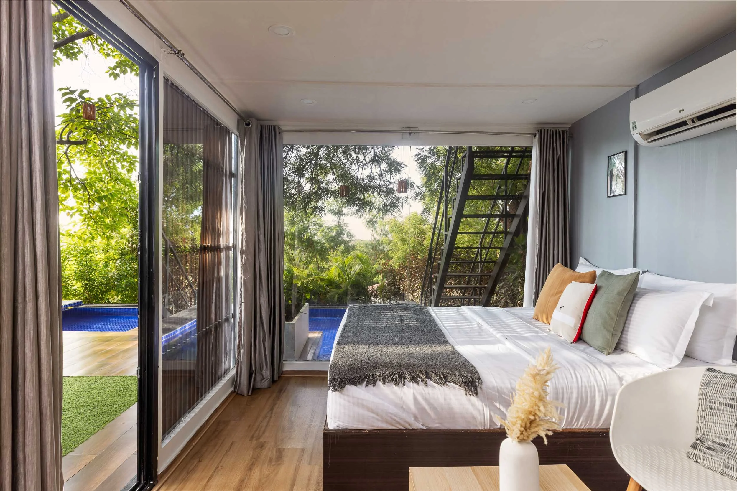 Interior daytime photography of a modern luxury staycation cabin in Hyderabad, featuring a bed, wooden flooring, and large glass sliding doors opening to a private plunge pool