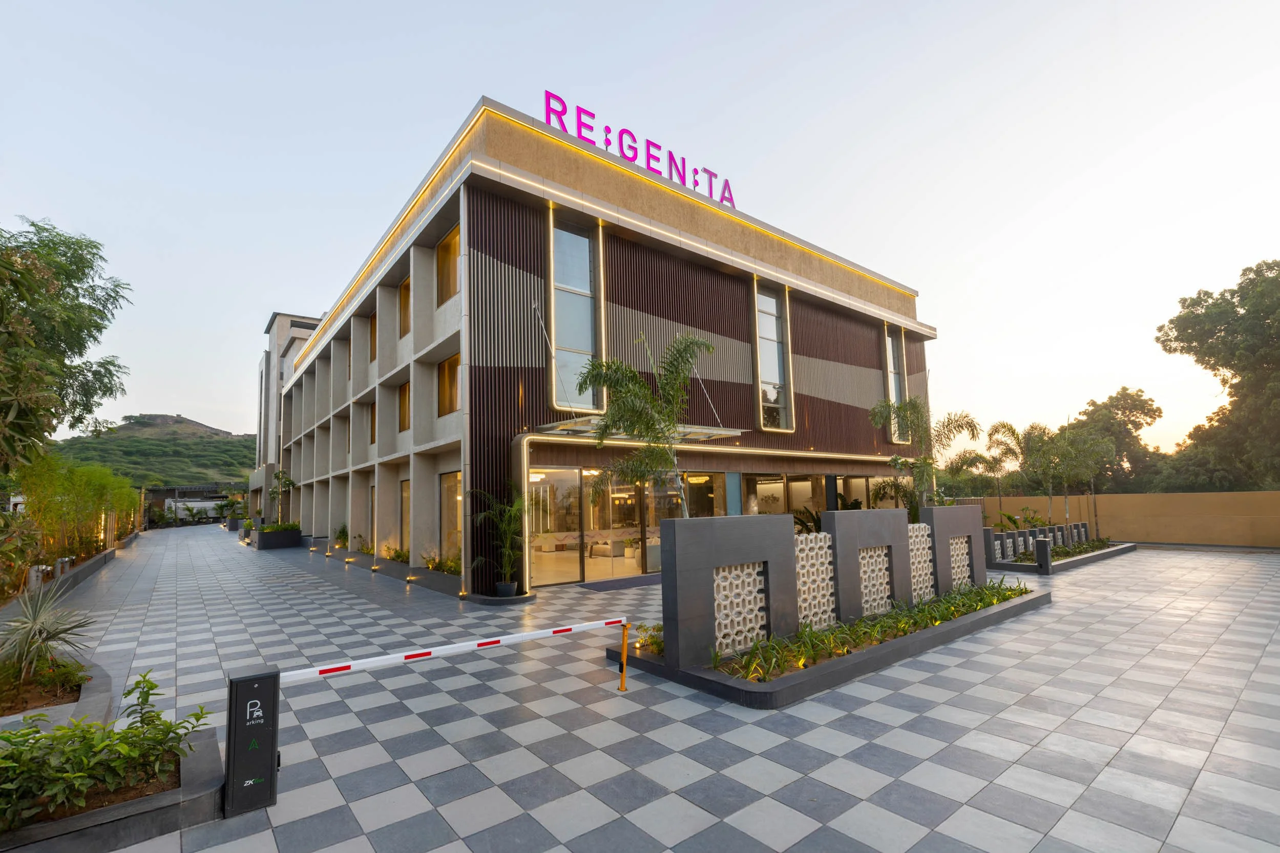Exterior daytime photography of the Regenta hotel featuring a modern facade with vertical louvers, a checkered patterned driveway, and clear blue skies