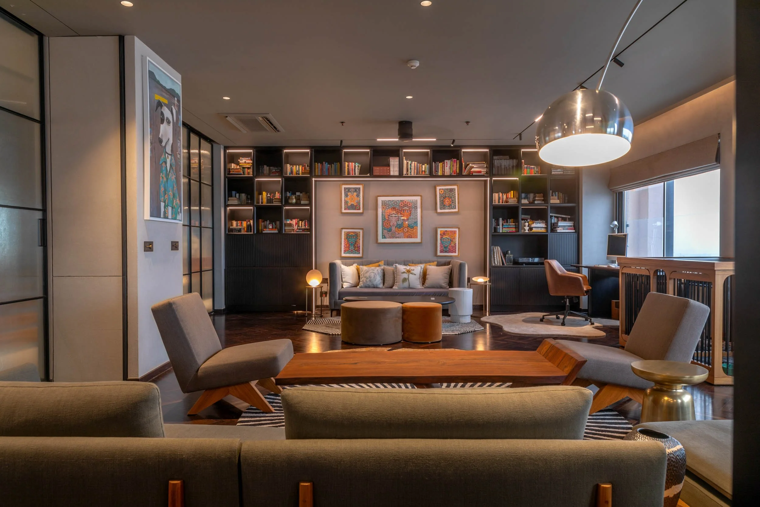 Interior photography of a modern living room featuring warm architectural lighting, a large grey sectional sofa, and an illuminated floor-to-ceiling bookshelf
