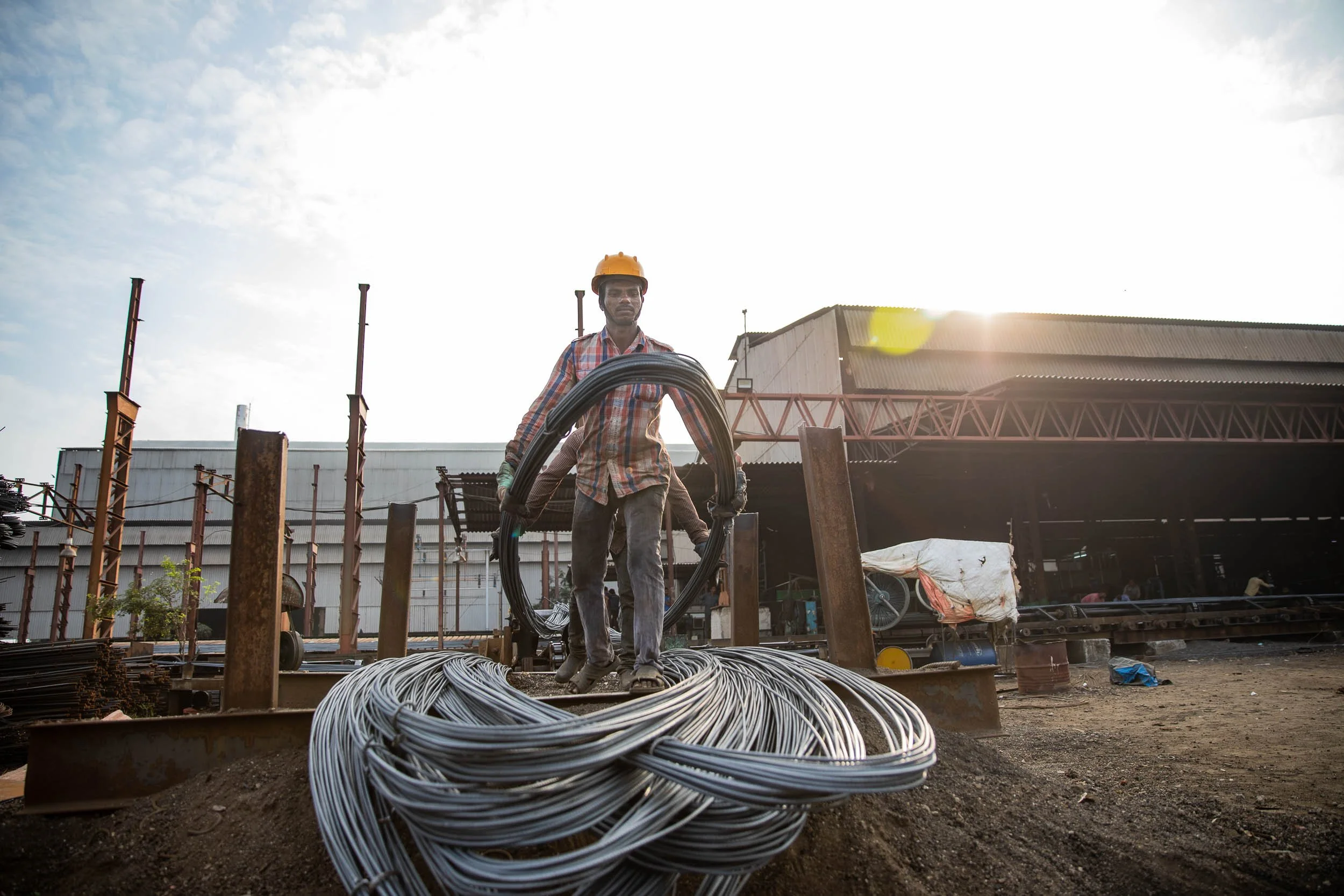 Exterior industrial photography of a worker standing with large spools of heavy metal wire rope at a manufacturing yard.