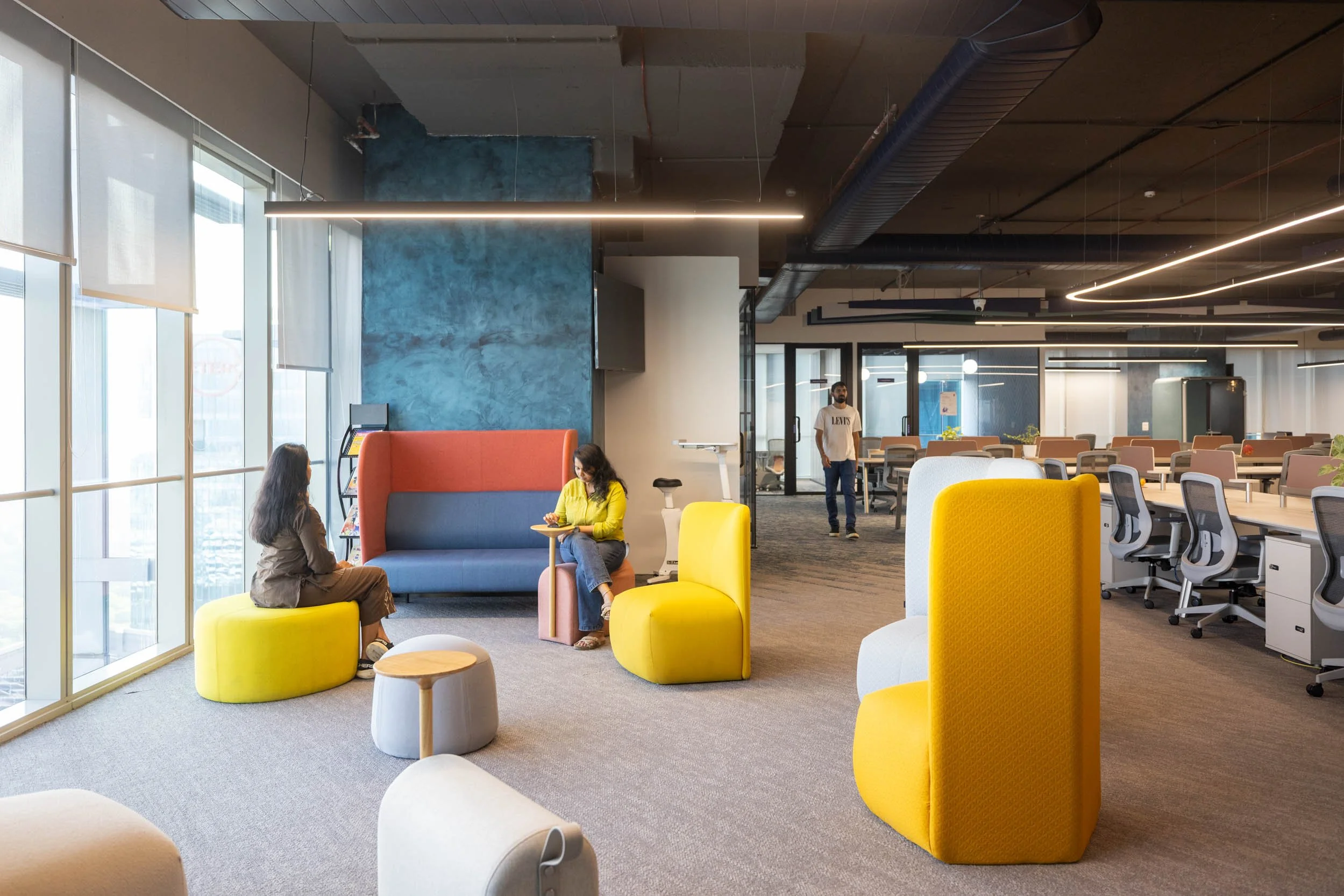 Commercial interior photography showcasing a dynamic corporate breakout area, highlighting modern open-plan office design, colorful ergonomic lounge seating, and industrial architectural elements