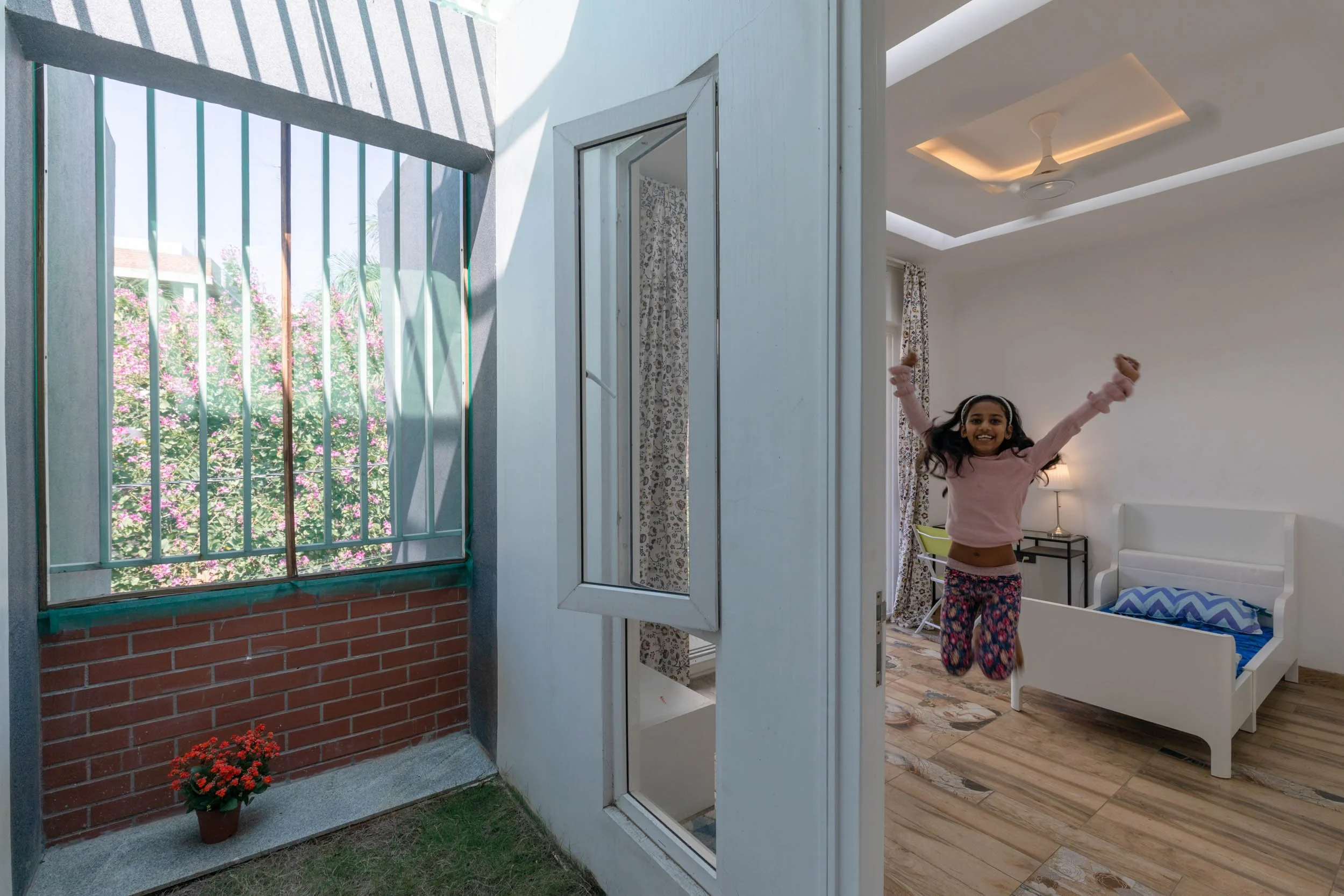 Professional residential architectural photography capturing a playful lifestyle moment, highlighting a seamless connection between a bright indoor space and a private brick balcony