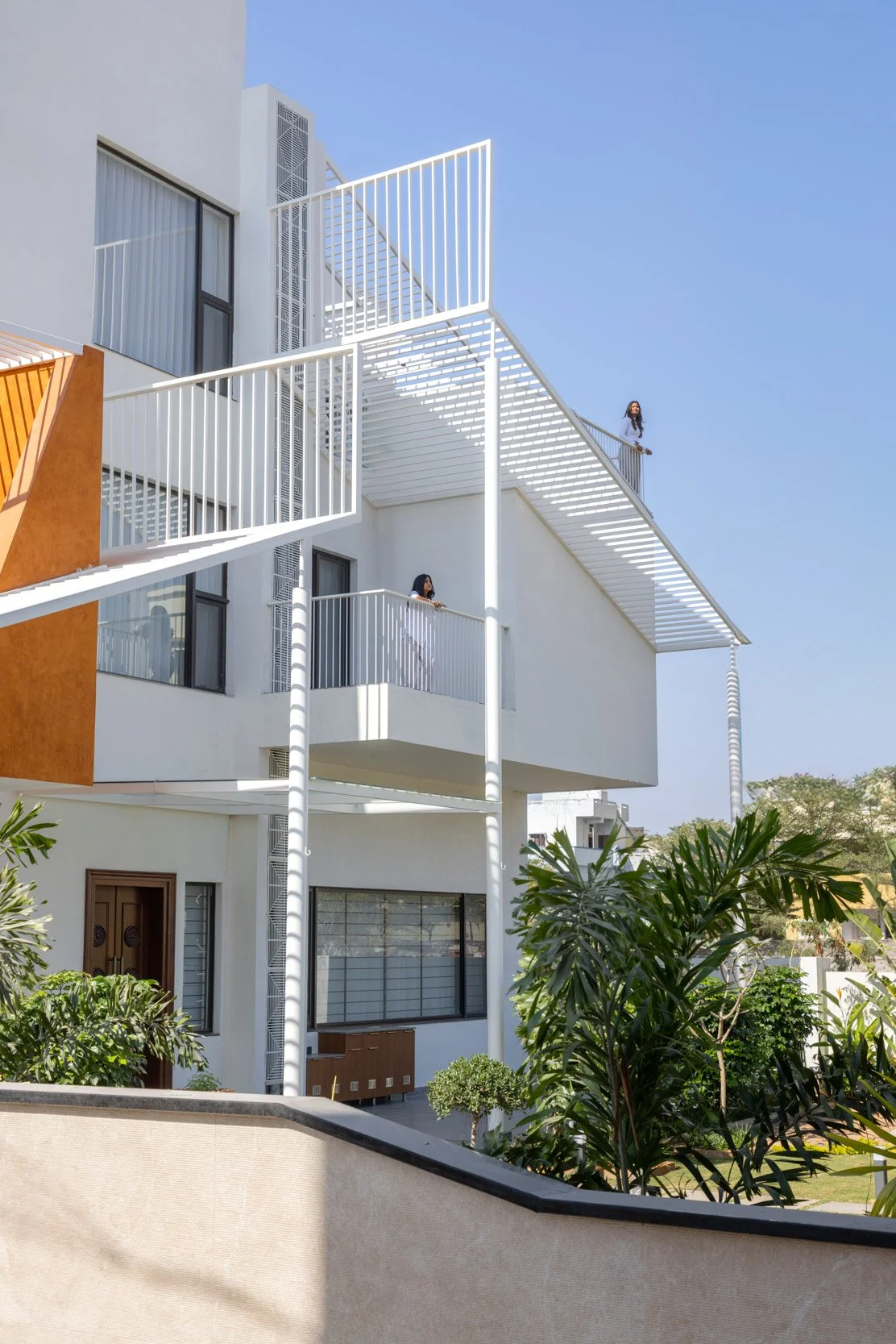 Professional exterior architectural photography of a modern residential home, featuring a shaded balcony and bold geometric terracotta accents.