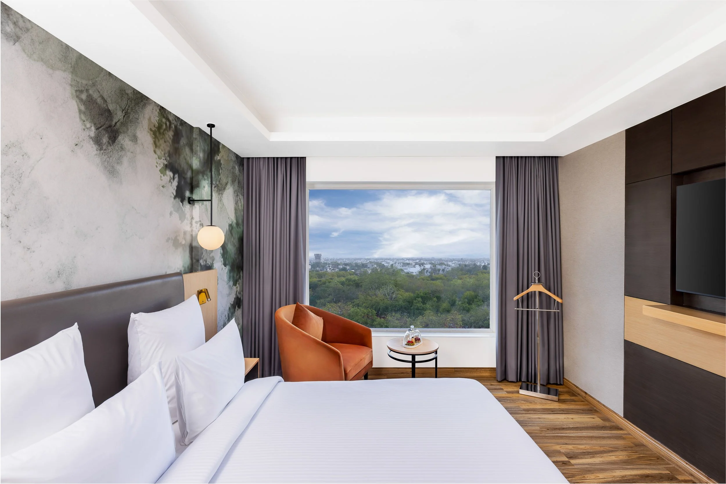 Interior photography of a bright, modern hotel bedroom featuring a custom wall mural, an orange accent armchair, and a large window with nature views