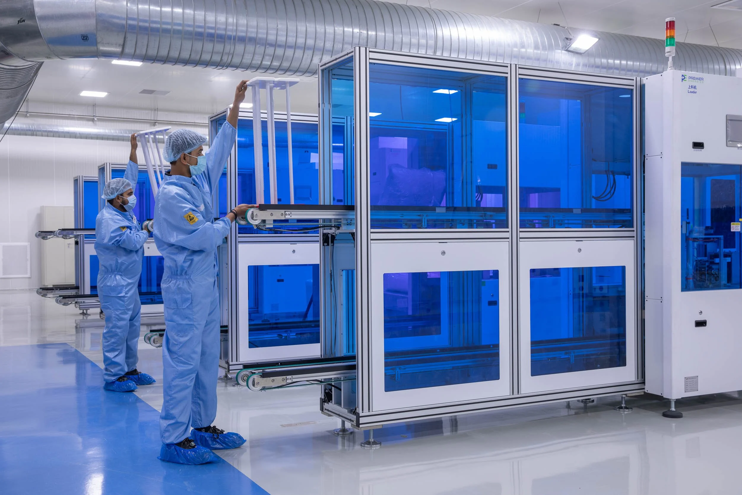 Interior industrial photography of workers in blue cleanroom suits operating specialized machinery in a sterile advanced manufacturing facility