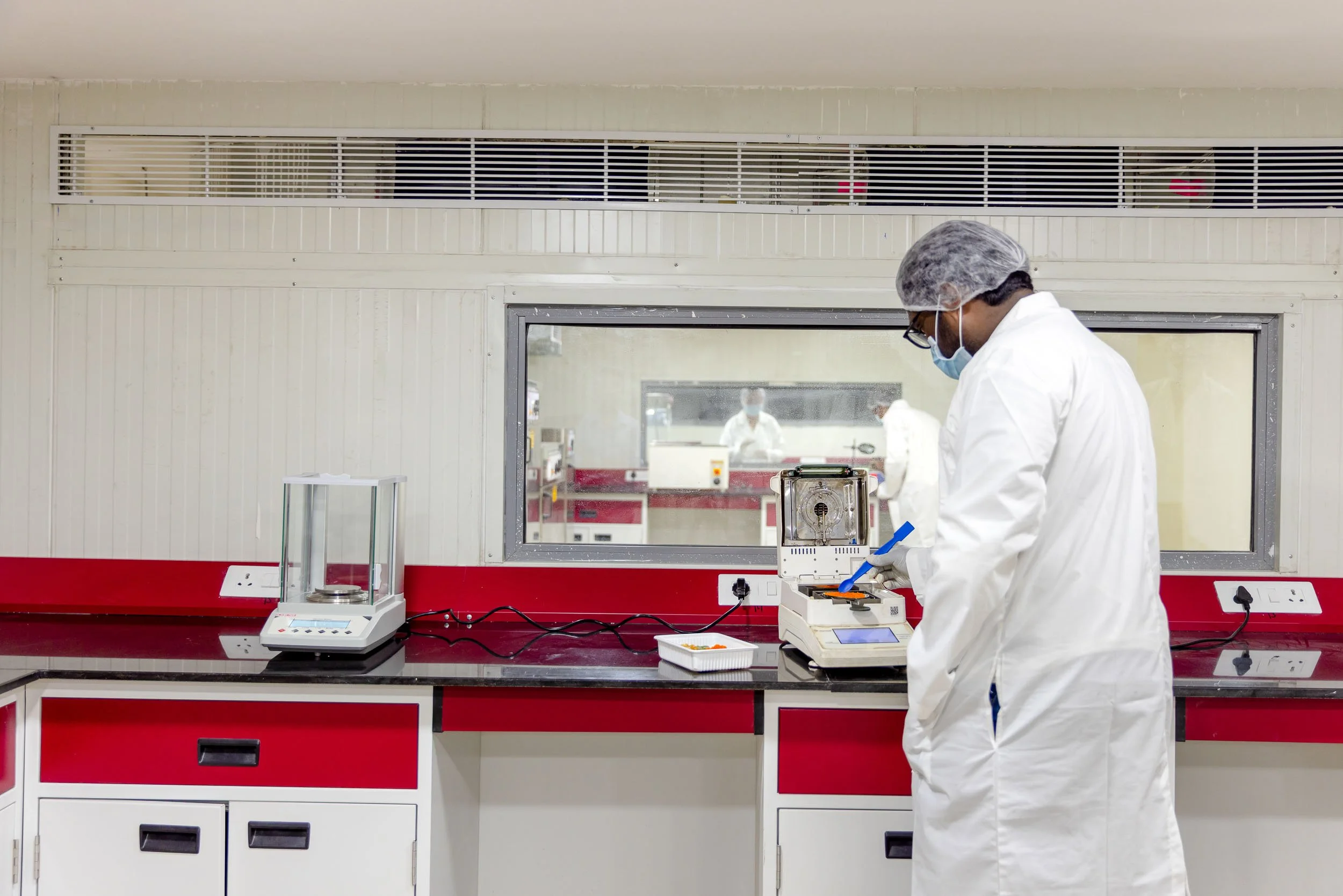 Interior industrial photography of a technician in a white lab coat conducting quality control testing in a bright, modern laboratory within a manufacturing facility
