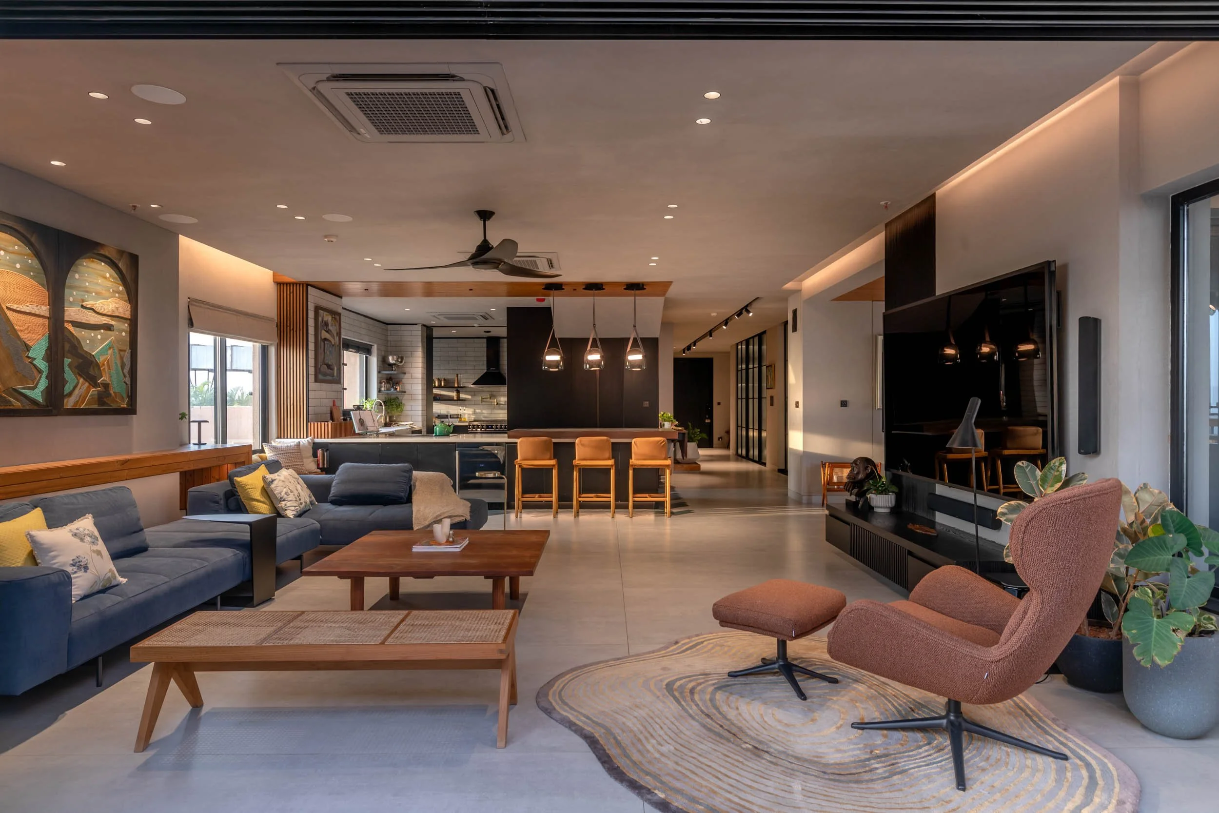 Wide interior shot of a modern open-plan living and dining room, featuring a blue sofa, wooden floors, and warm architectural ceiling lighting