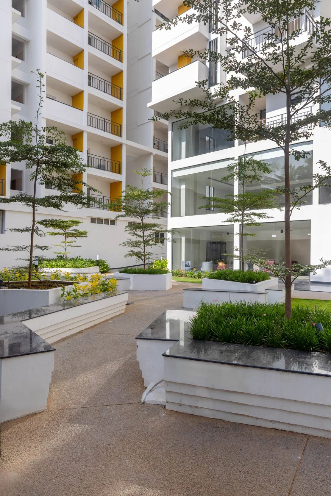 Residential real estate exterior photography featuring a modern apartment building with colorful balcony details, paved pedestrian walkways, and integrated green landscaping