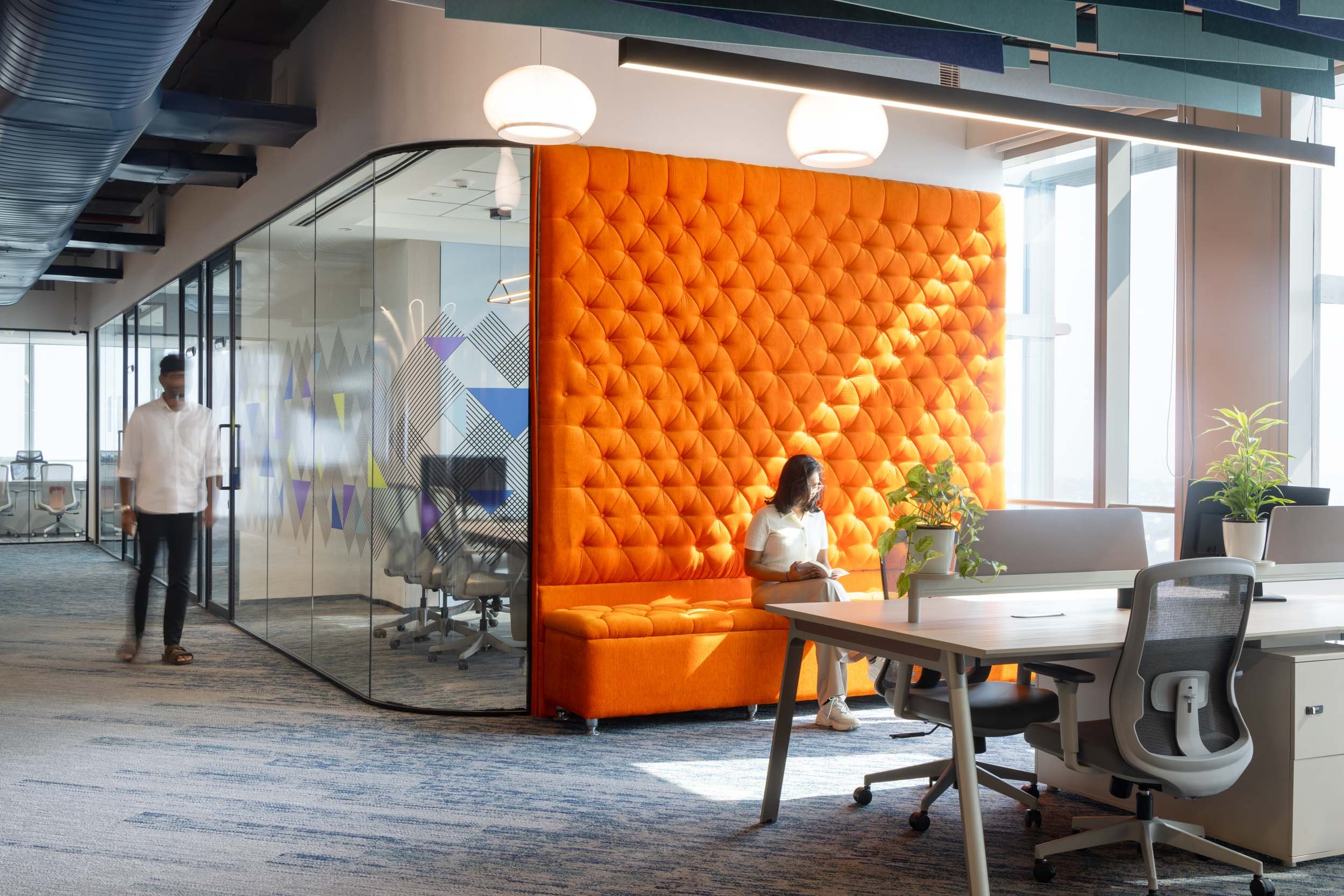 Commercial interior photography showcasing a dynamic corporate workspace, highlighting bold orange acoustic wall panels, glass-enclosed meeting rooms, and open-plan desk arrangements