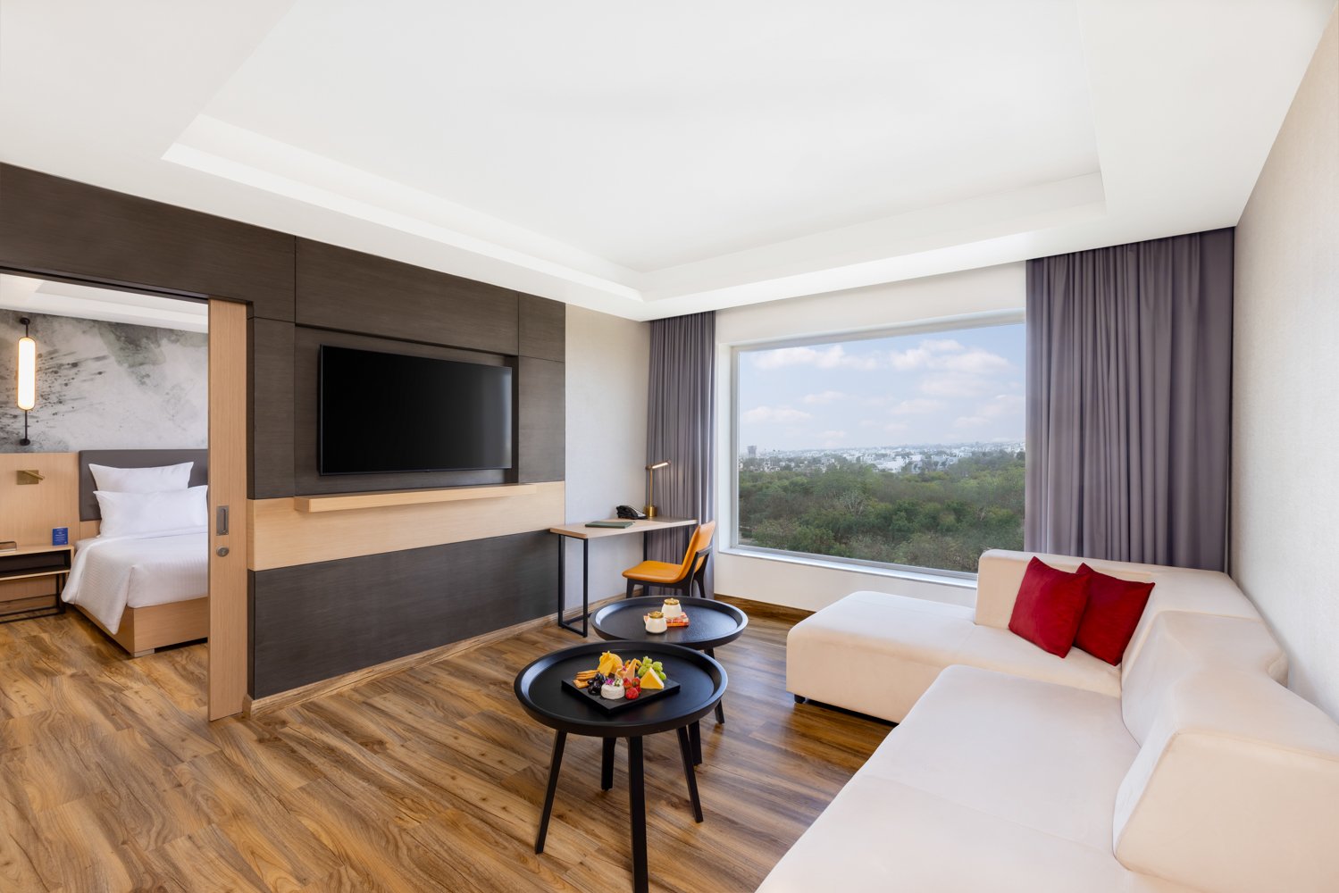 Interior photography of a bright, modern hotel bedroom featuring a large bed, wooden flooring, a cozy seating area, and large windows with a nature view