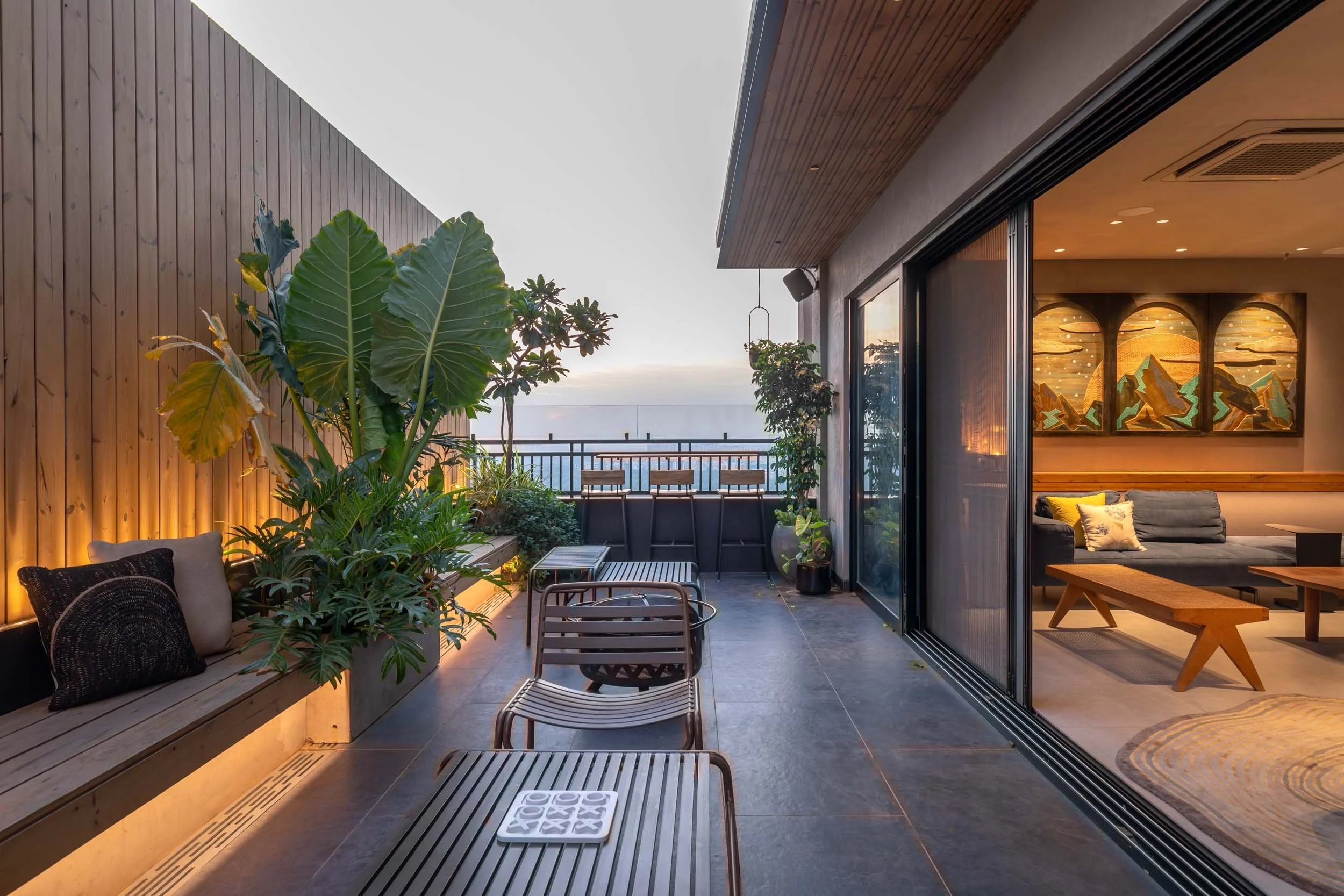 Modern outdoor balcony terrace at twilight featuring warm architectural lighting, comfortable seating, and large glass sliding doors