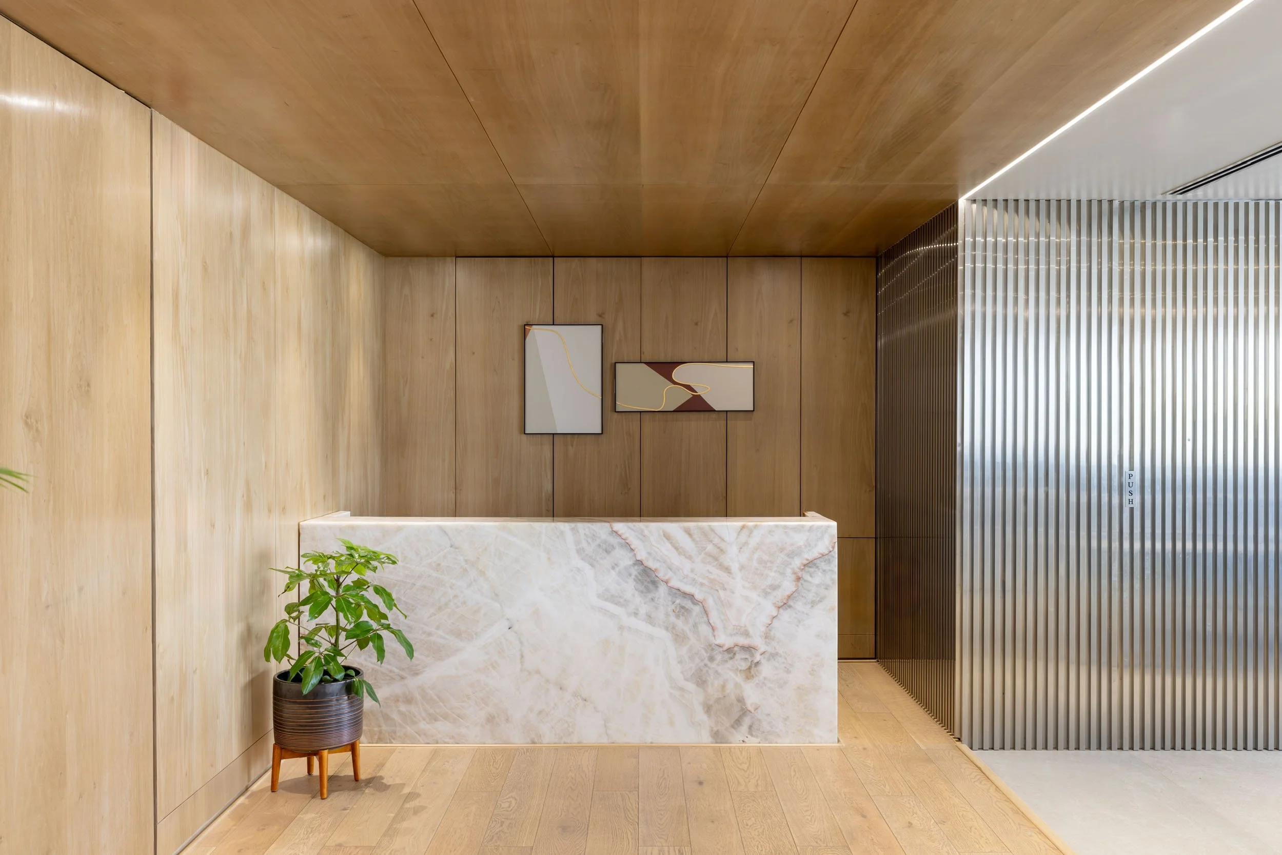 Commercial interior photography showcasing a modern office reception space, highlighting custom marble desk design, warm architectural wood paneling, and contemporary entryways