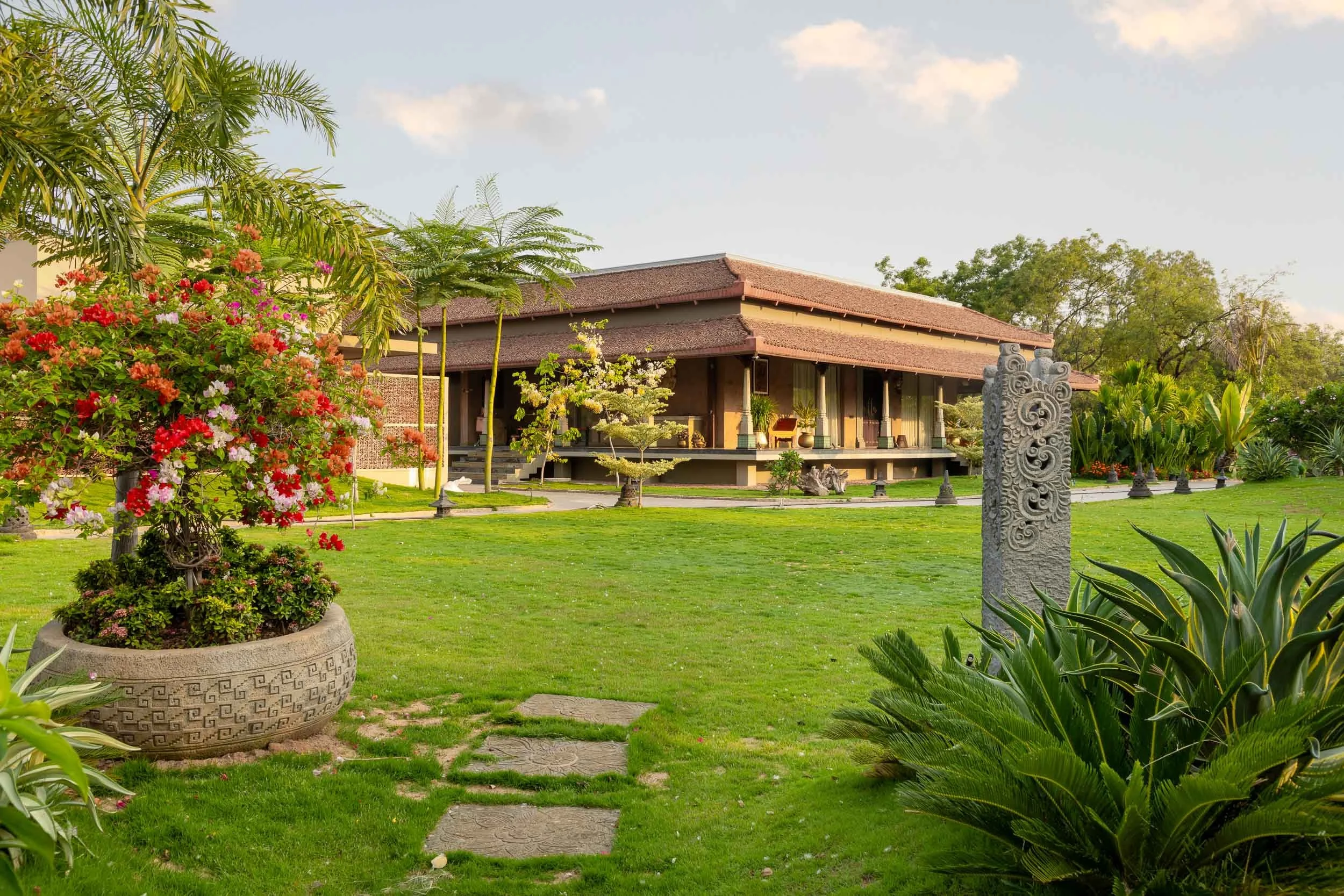 Wide landscape photography of a luxury resort featuring a sprawling green lawn, mature shade trees on the left, and a traditional building in the distance