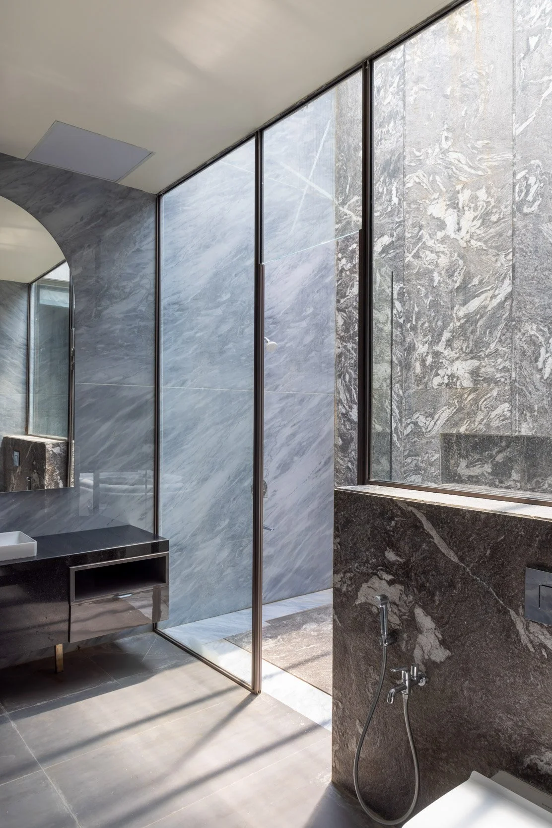 Professional interior architectural photography of a modern residential space, highlighting beautiful natural light filtering through large glass windows onto elegant dark stone fixtures
