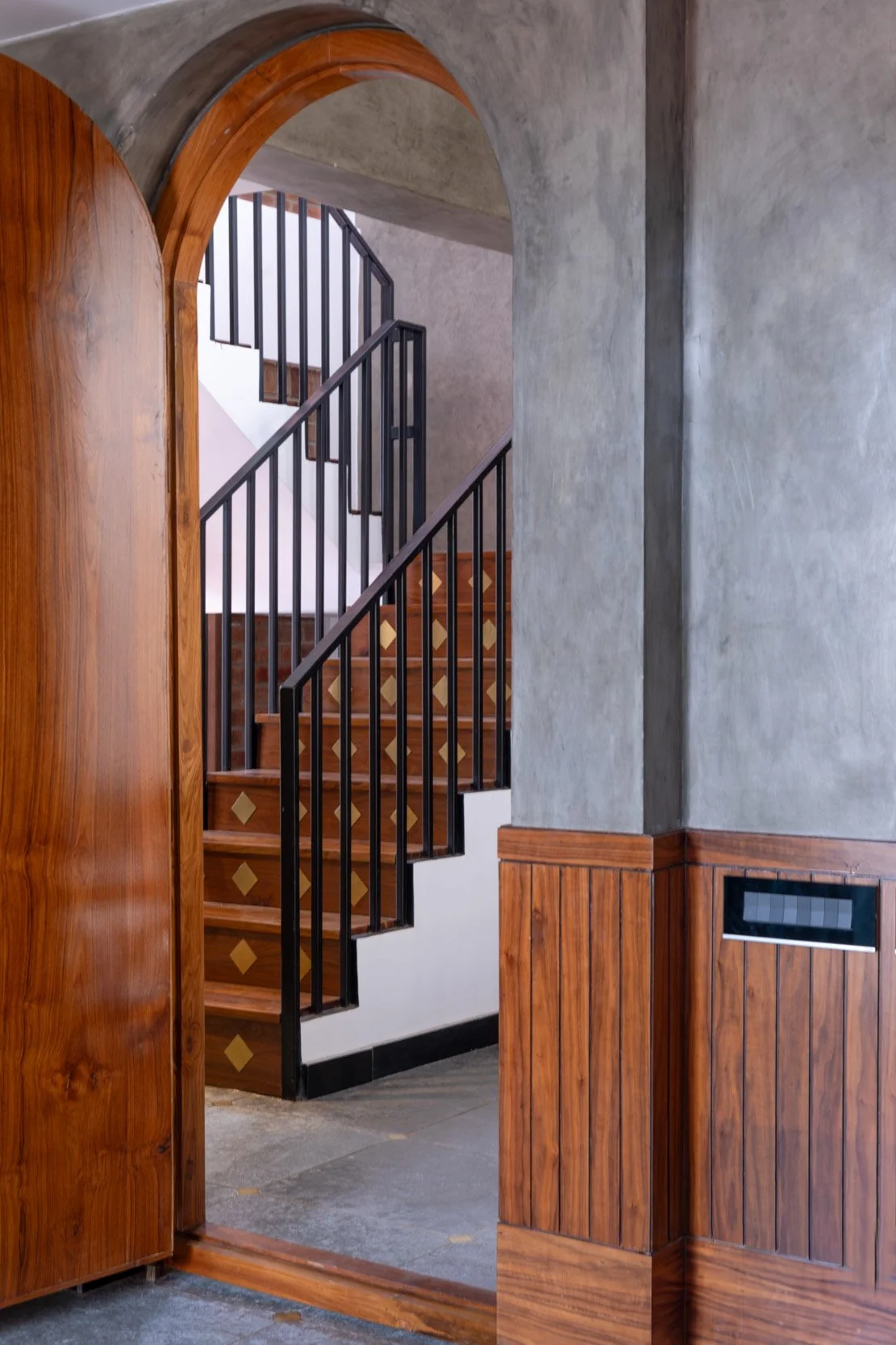 Professional interior architectural photography of a modern residential home, highlighting an elegant wooden arched doorway framing a classic staircase