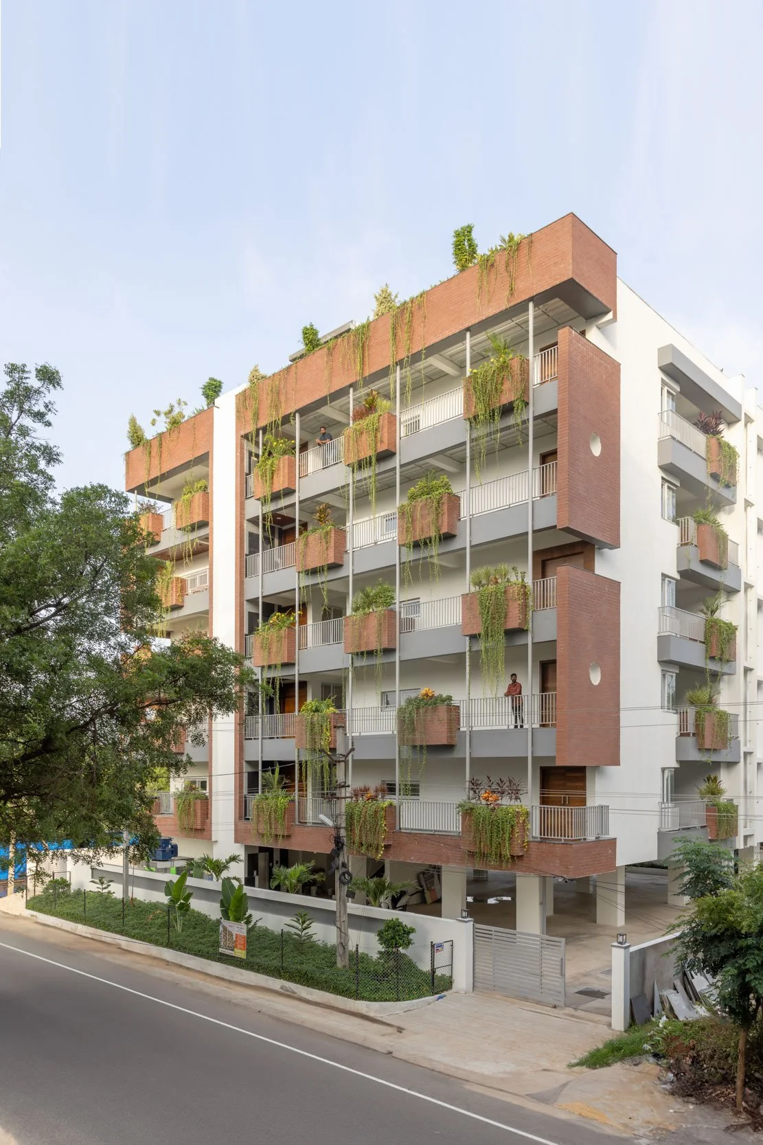 Professional exterior architectural photography of a modern mid-rise building, capturing a street-level perspective and highlighting a beautiful biophilic facade with lush balcony gardens