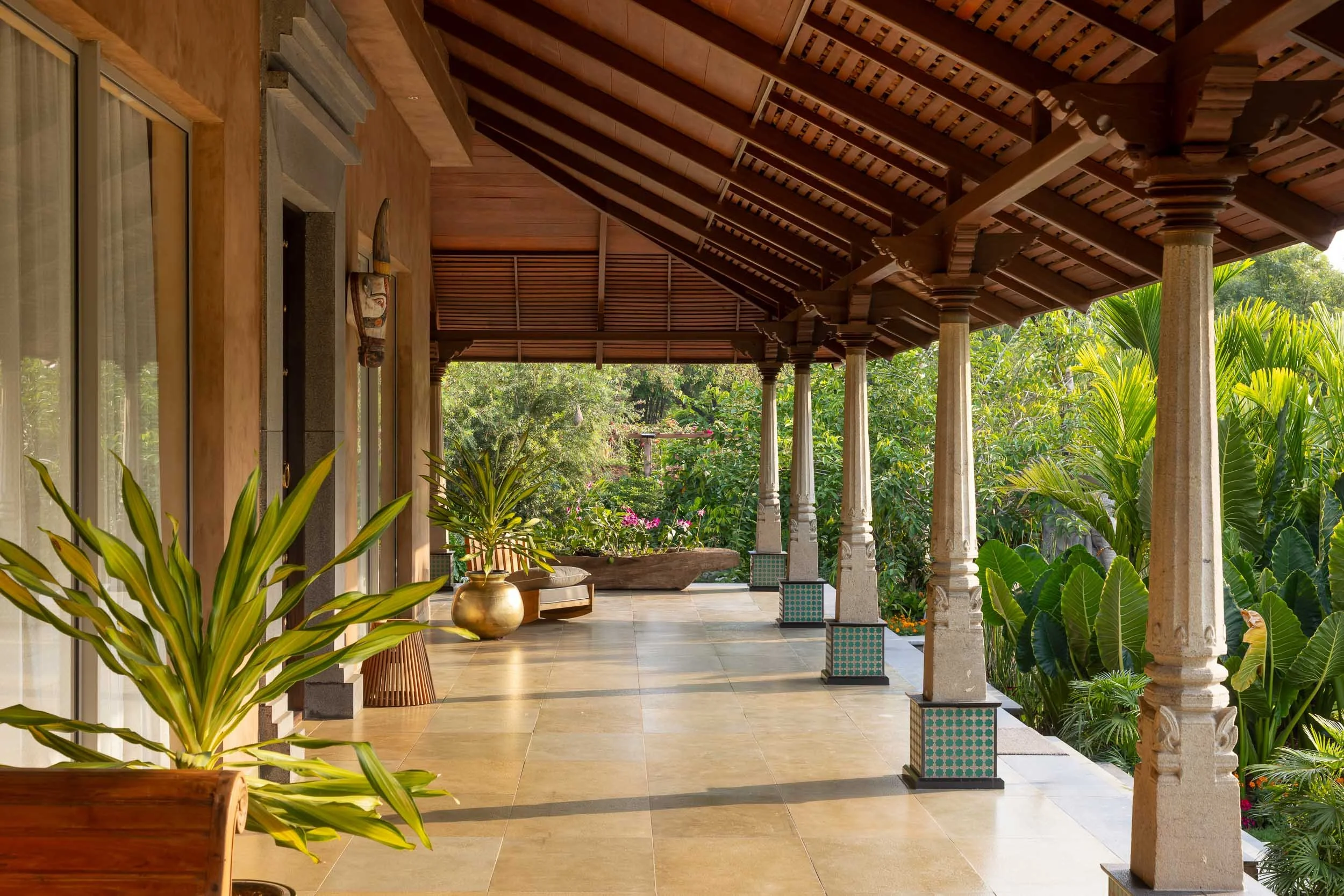 Exterior daytime photography of a luxury resort farm stay featuring a traditional building with a pitched roof, wooden veranda pillars, and a stone pathway across a manicured green lawn